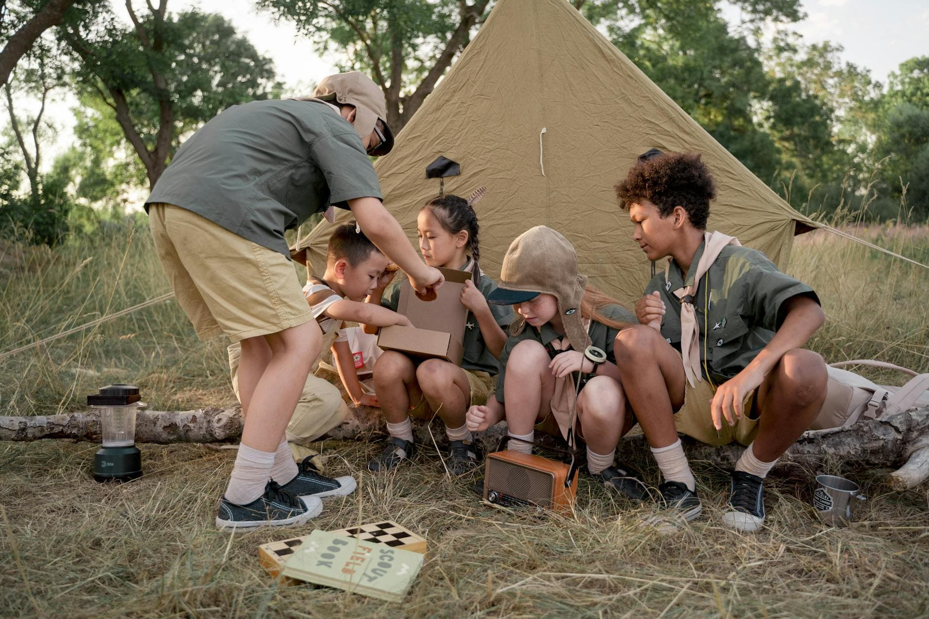 A group of young scouts gathers around a tent, exploring and bonding during a summer camping trip. - outdoor social skills