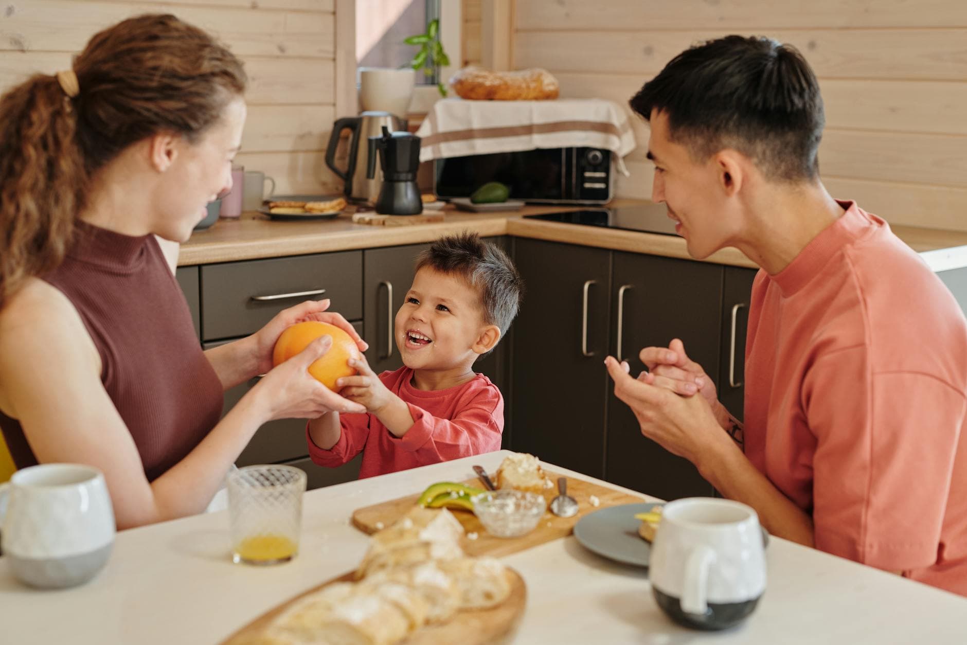 Joyful family breakfast with smiling child sharing orange indoors in cozy kitchen. - partner communication family