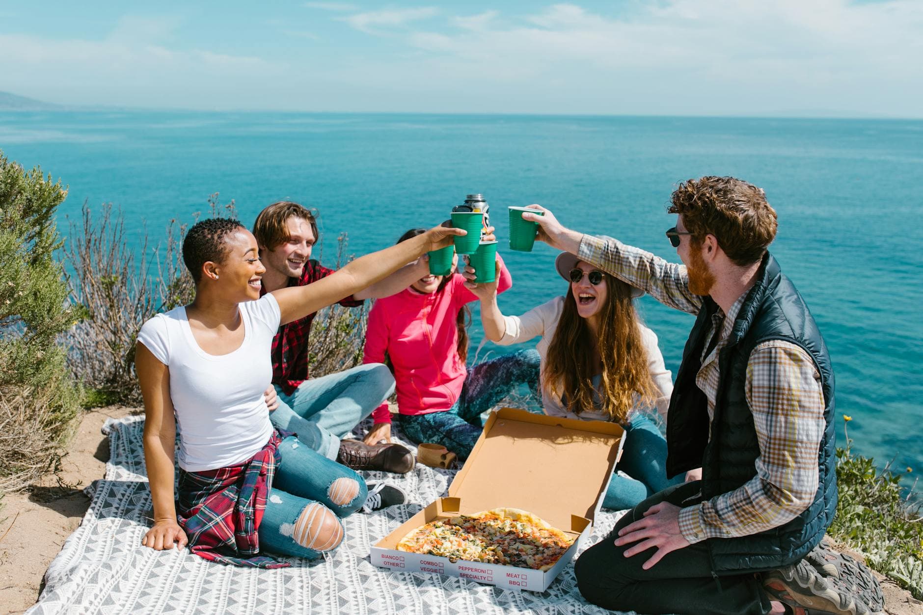 Group of friends having a joyful picnic by the ocean with pizza and drinks. - post spring break reconnect