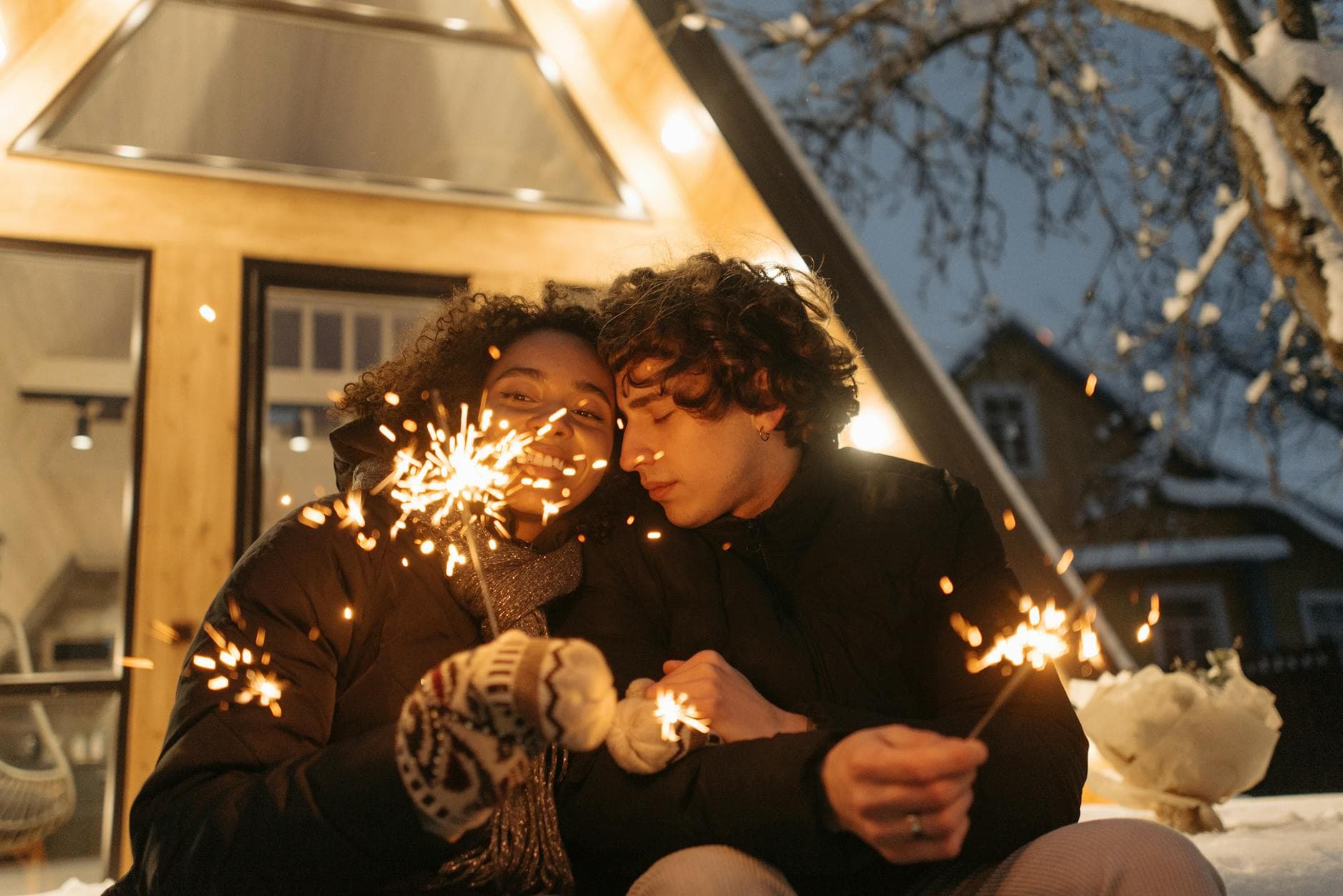 Happy couple holding sparklers outside a cozy cabin in winter, creating a festive atmosphere. - reignite relationship spark