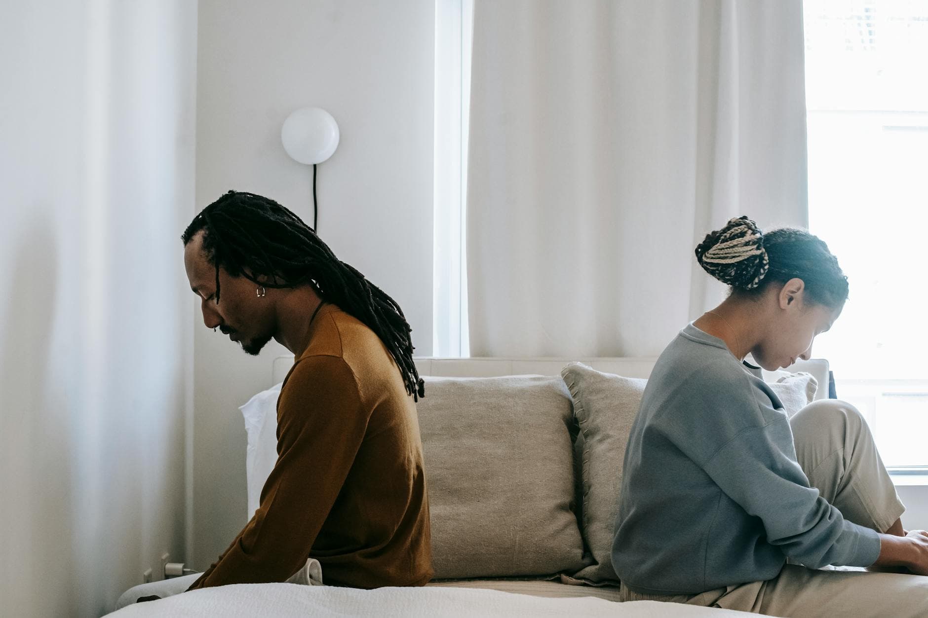 Side view unhappy sorrowful African American couple sitting on bed back to back after having argument - relationship resentment