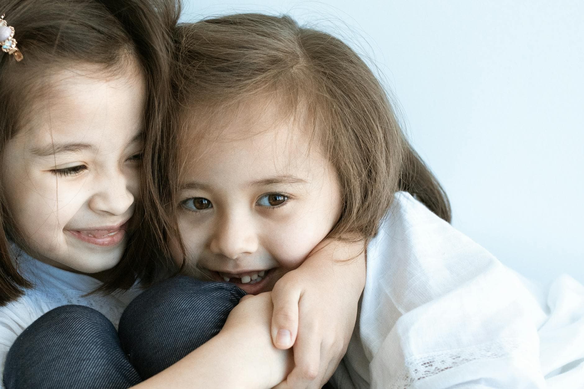 Two young girls hugging and smiling warmly indoors, expressing happiness and love. - sibling rivalry definition