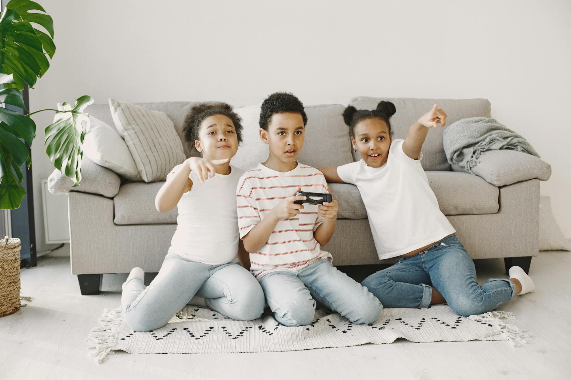Children sitting on a rug, playing video games and pointing excitedly in a cozy living room. - sibling rivalry quotes