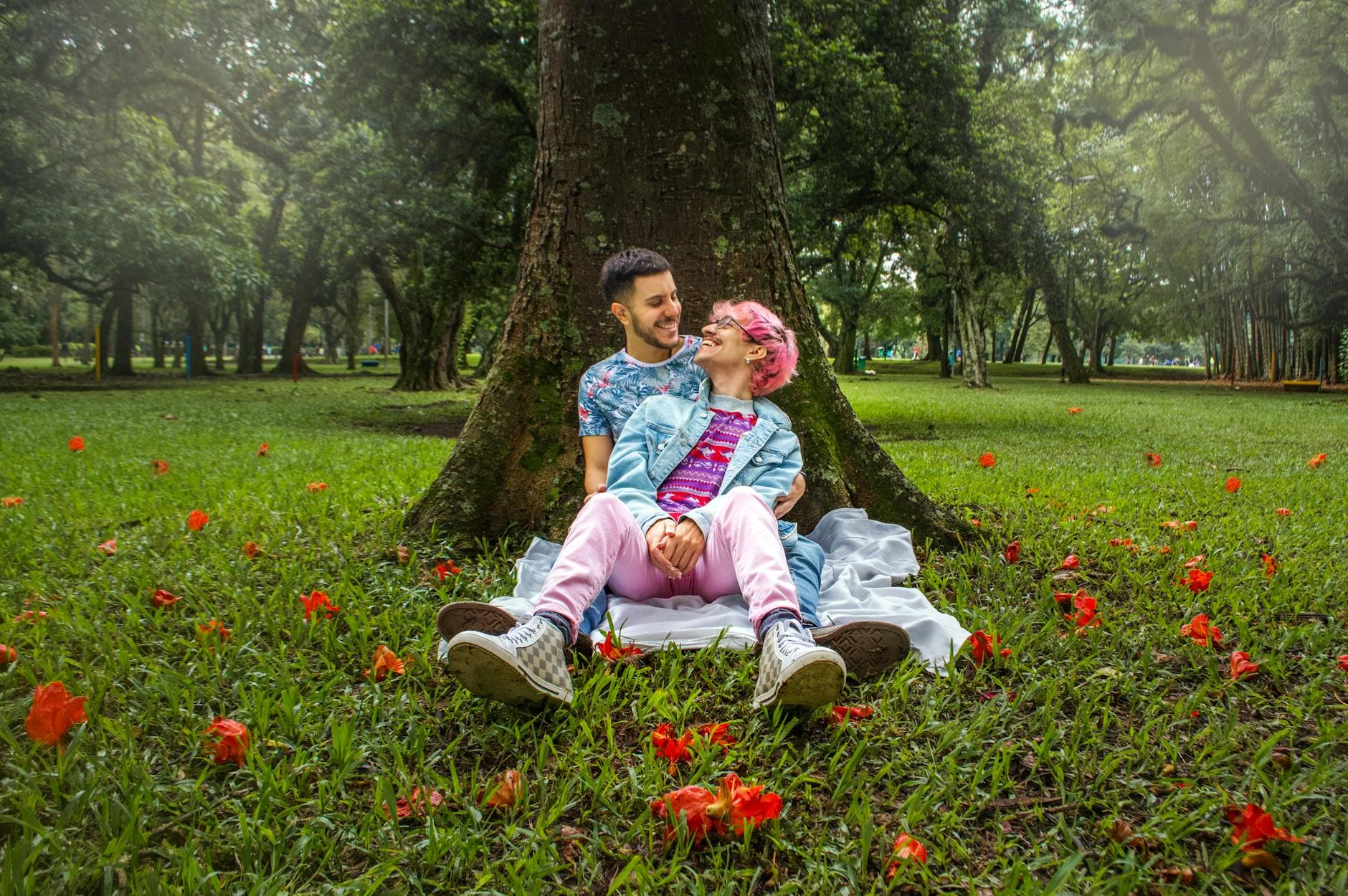 A joyful couple sits together on a picnic blanket in a lush green park surrounded by vibrant flowers. - spring dating ideas