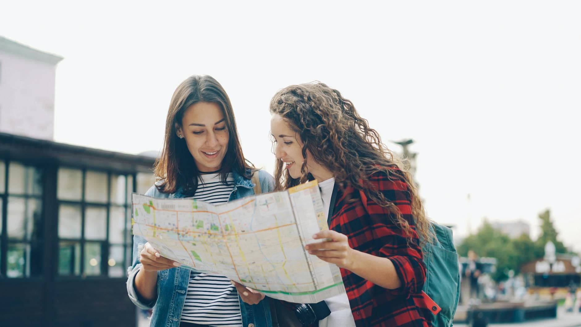 Two women exploring a city with a map, enjoying a sunny outdoor day. - summer vacation planning