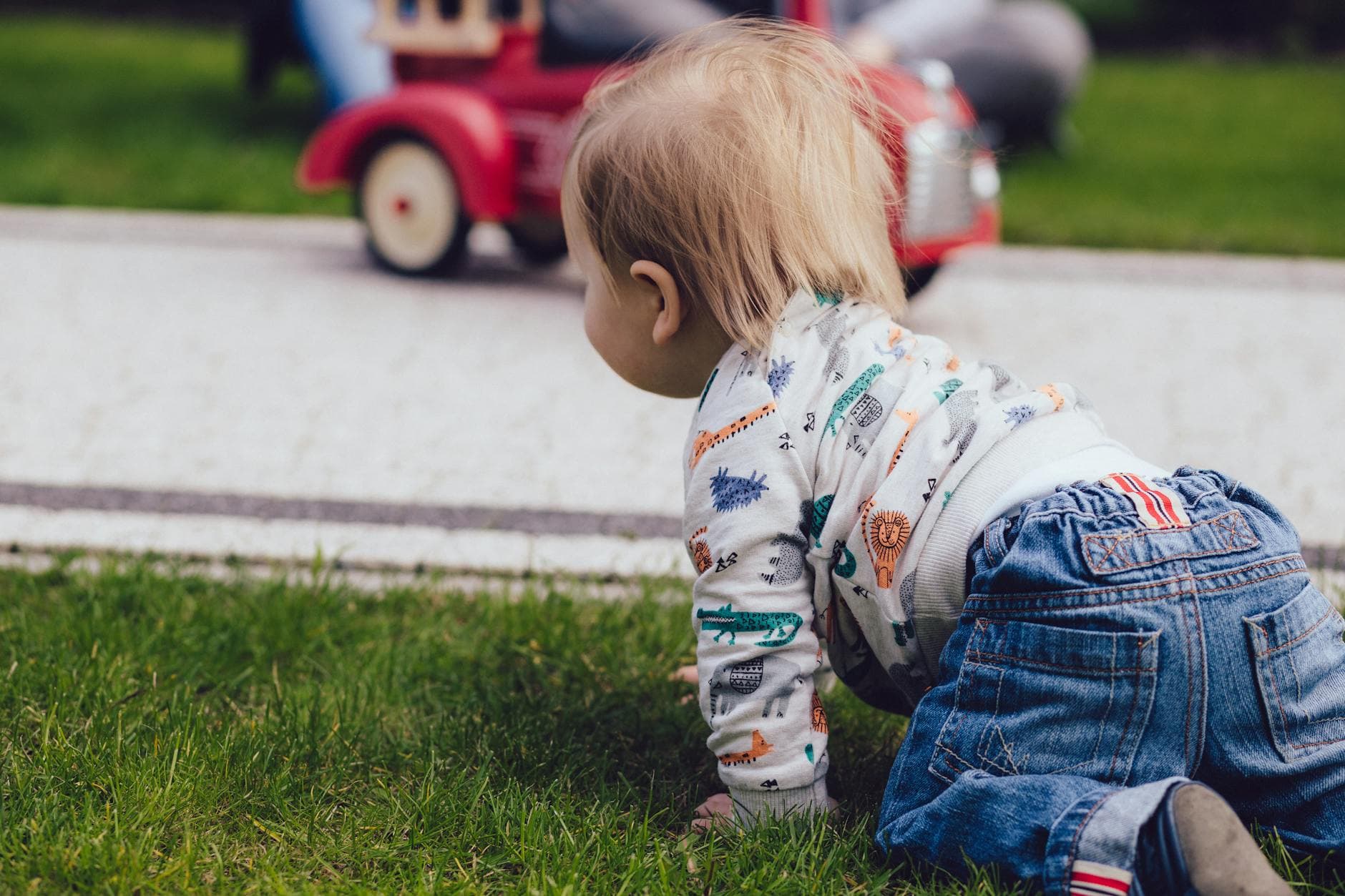 A toddler crawling on green grass outdoors near a toy car, enjoying a sunny day. - toddler tantrums outdoors