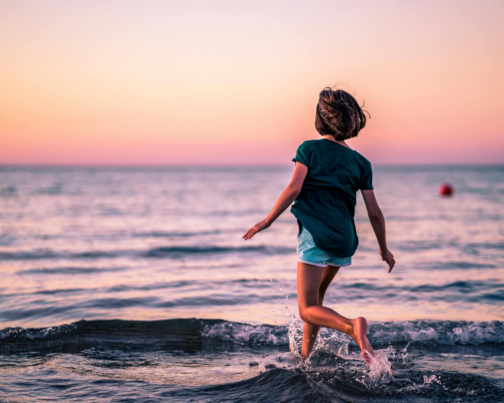 Back view of unrecognizable little girl with bare feet running in sea at sunset in summer vacation - child resilience summer