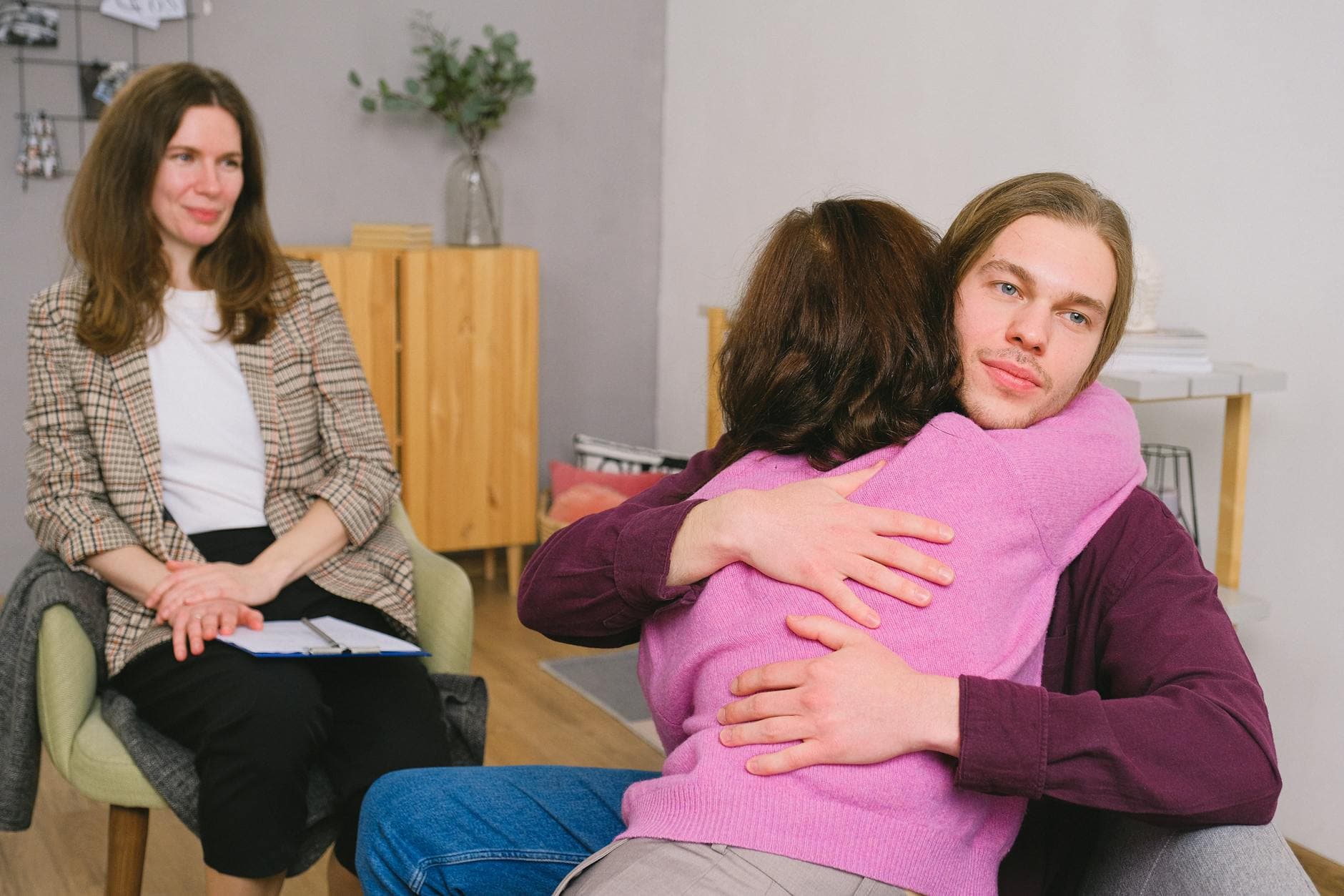 Calm couple in casual clothes sitting and embracing during session with psychologist in light room with wooden furniture - couples therapy goals
