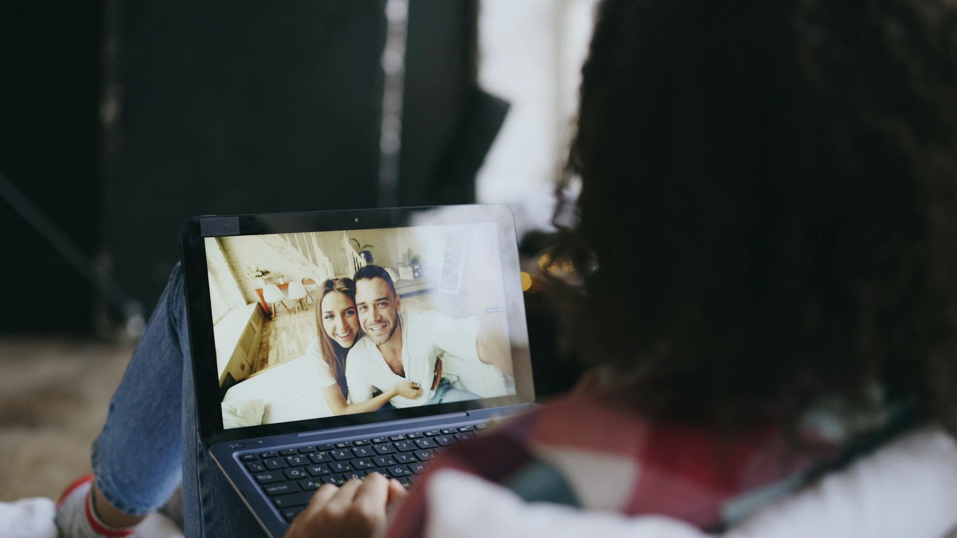 Woman viewing a happy couple's photo on a laptop at home, suggesting connection through technology. - deep couple communication