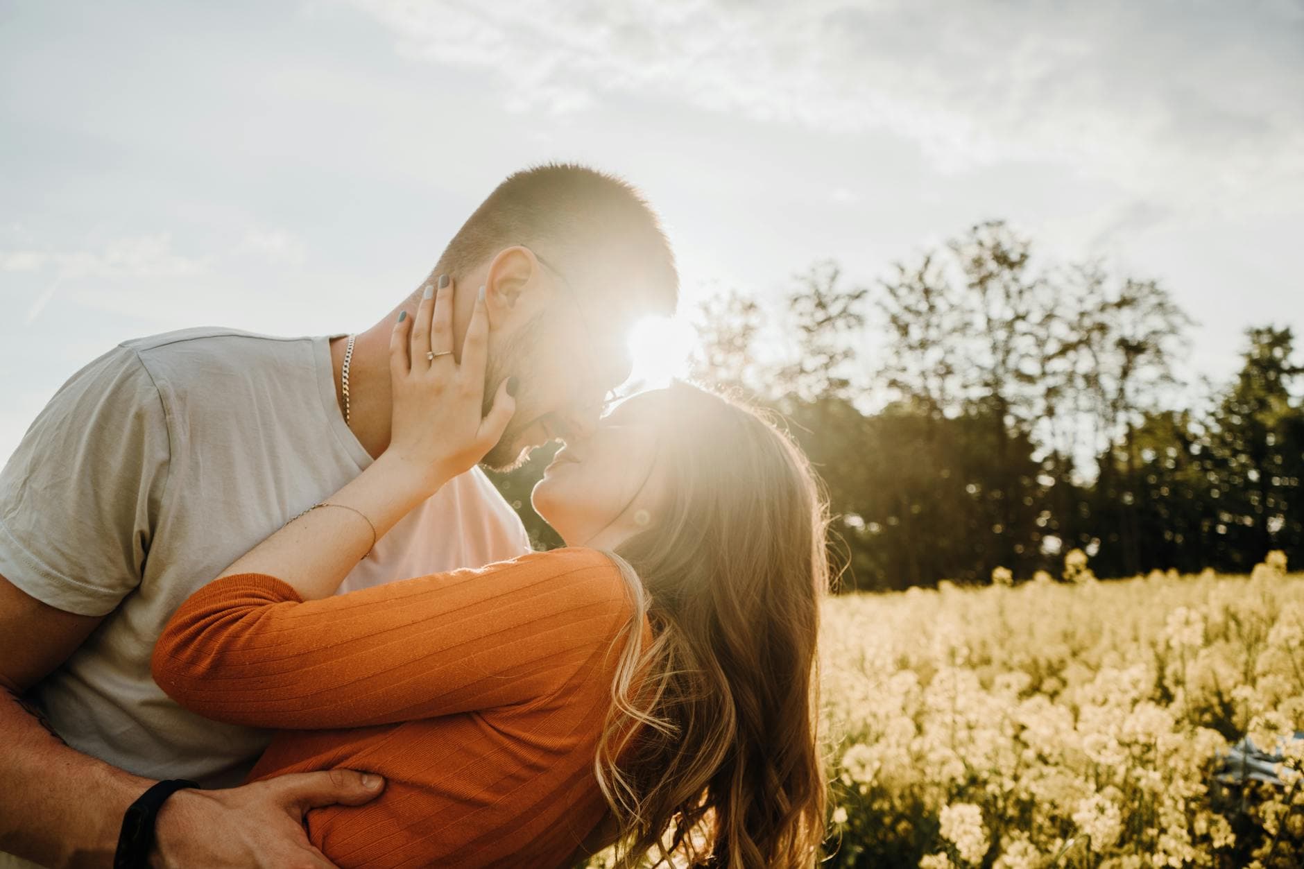 A couple shares a romantic embrace in a sunlit field with flowers and trees. - deepen relationship spring