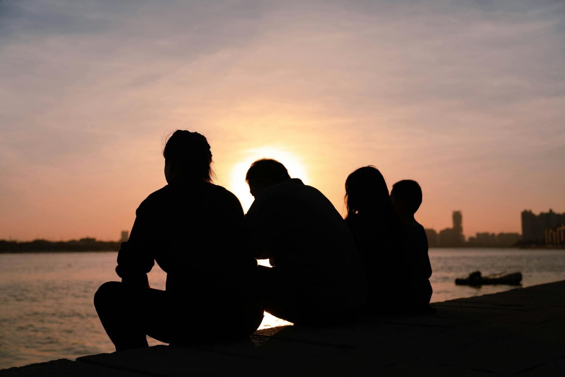 Silhouette of a family sitting by the water during a serene sunset, evoking tranquility and togetherness. - family communication empathy