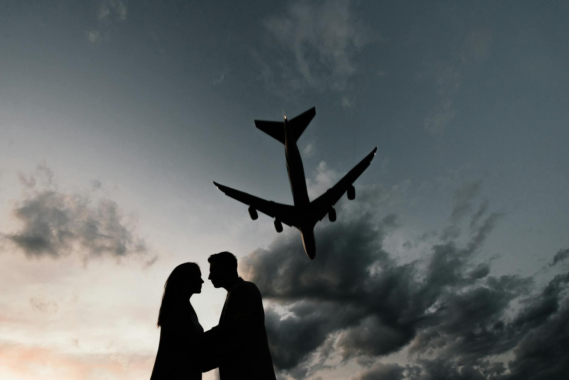 Romantic silhouette of a couple embracing with an airplane overhead during a dramatic sunset. - long distance relationship tips