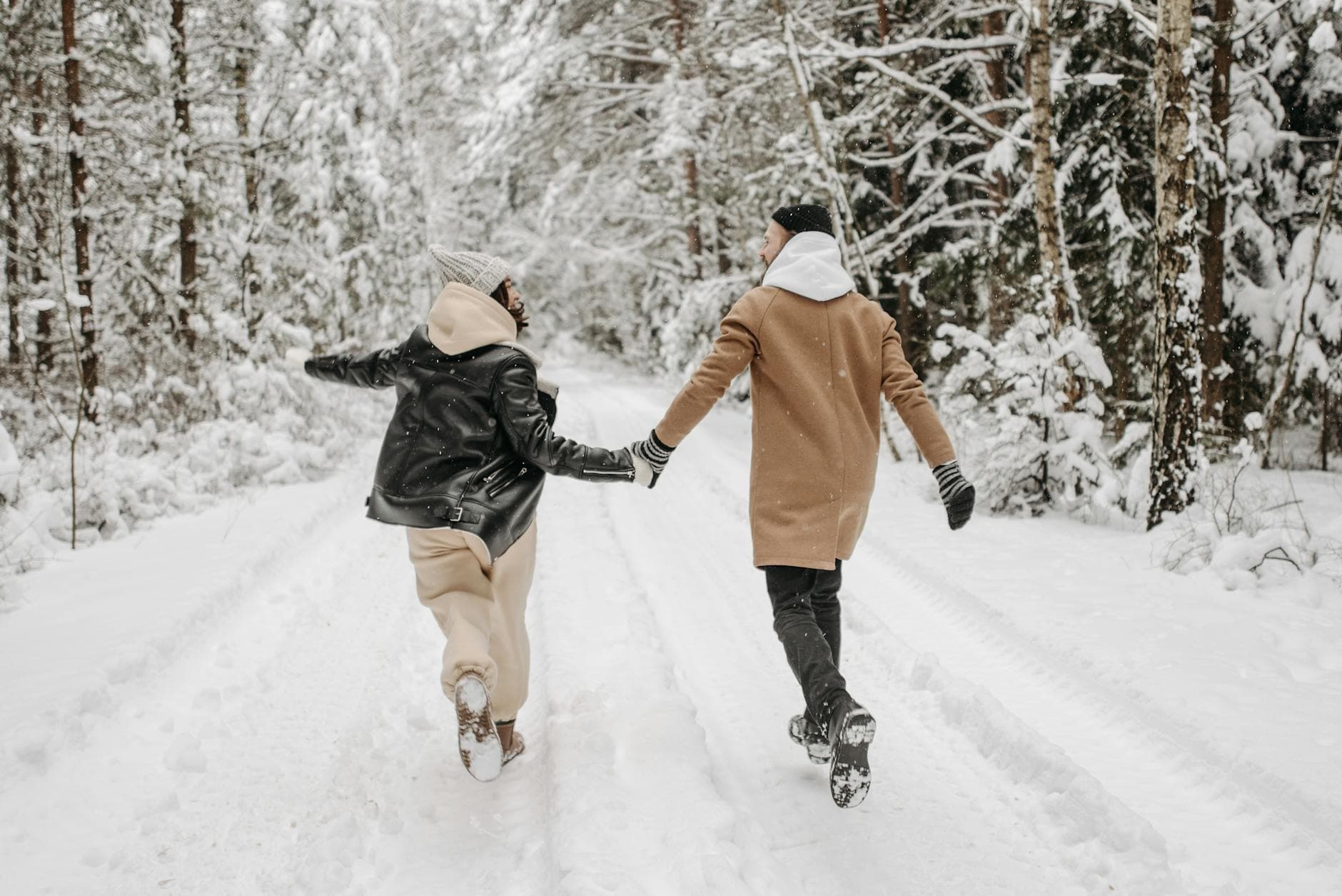 A couple joyfully runs through a snowy forest, holding hands in the winter season. - marriage after winter