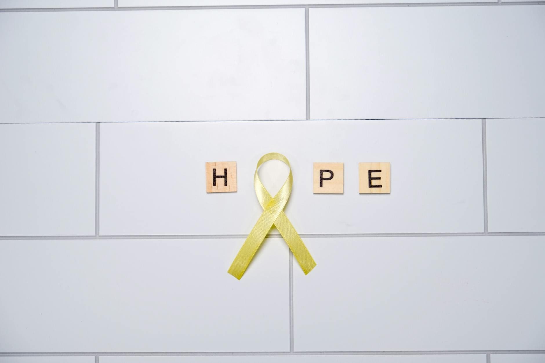 A yellow ribbon forming the word 'hope' with tiles on a white tiled background, symbolizing awareness and support. - mental health reset