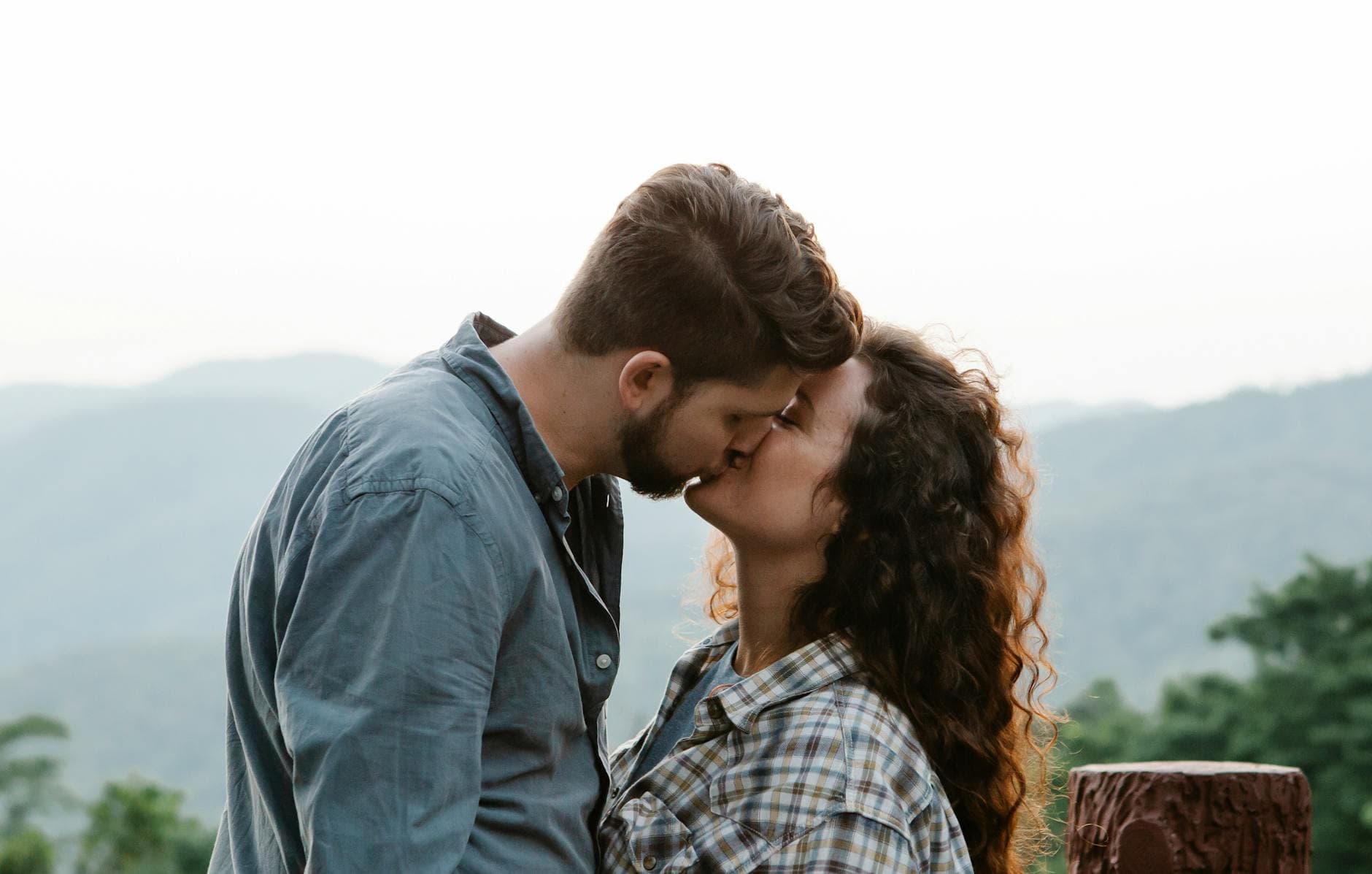 Side view of young loving couple in casual outfits kissing each other during romantic date in mountainous countryside - relationship check in