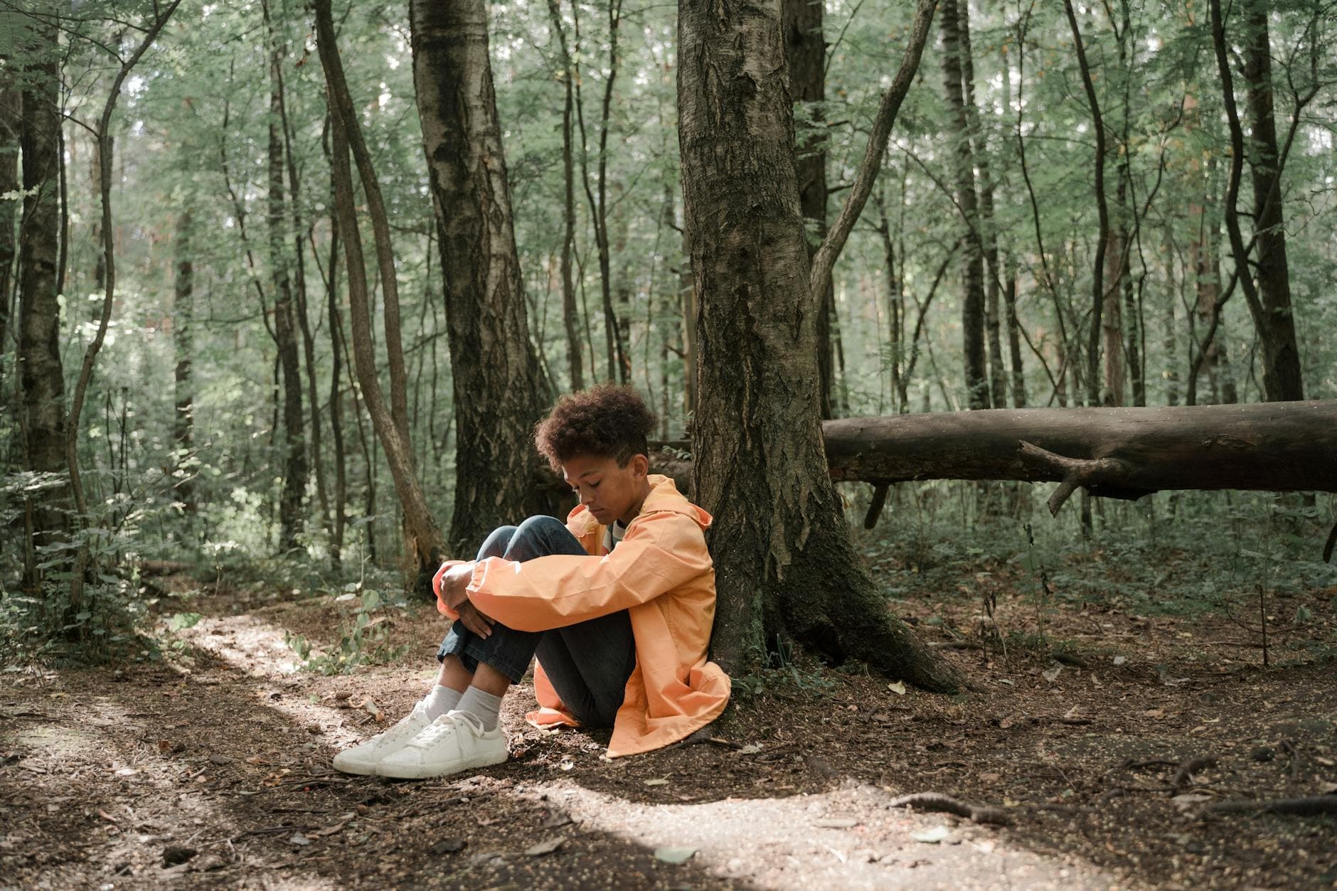 A young boy in a bright jacket sits alone in a serene forest, evoking emotions of solitude and reflection. - seasonal depression treatment