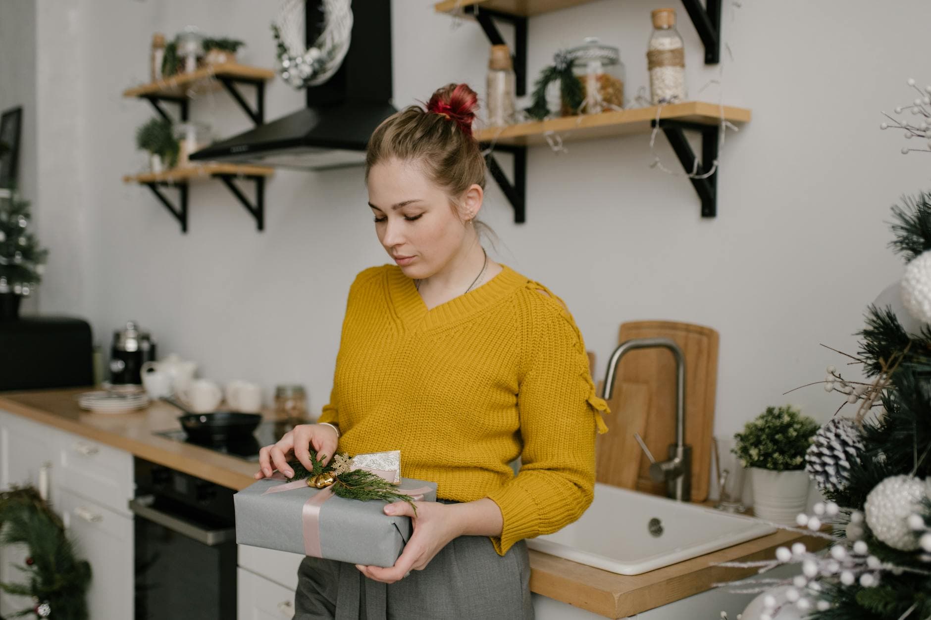 Young woman in yellow sweater holding a gift box in a cozy, decorated kitchen during winter. - seasonal mood boost