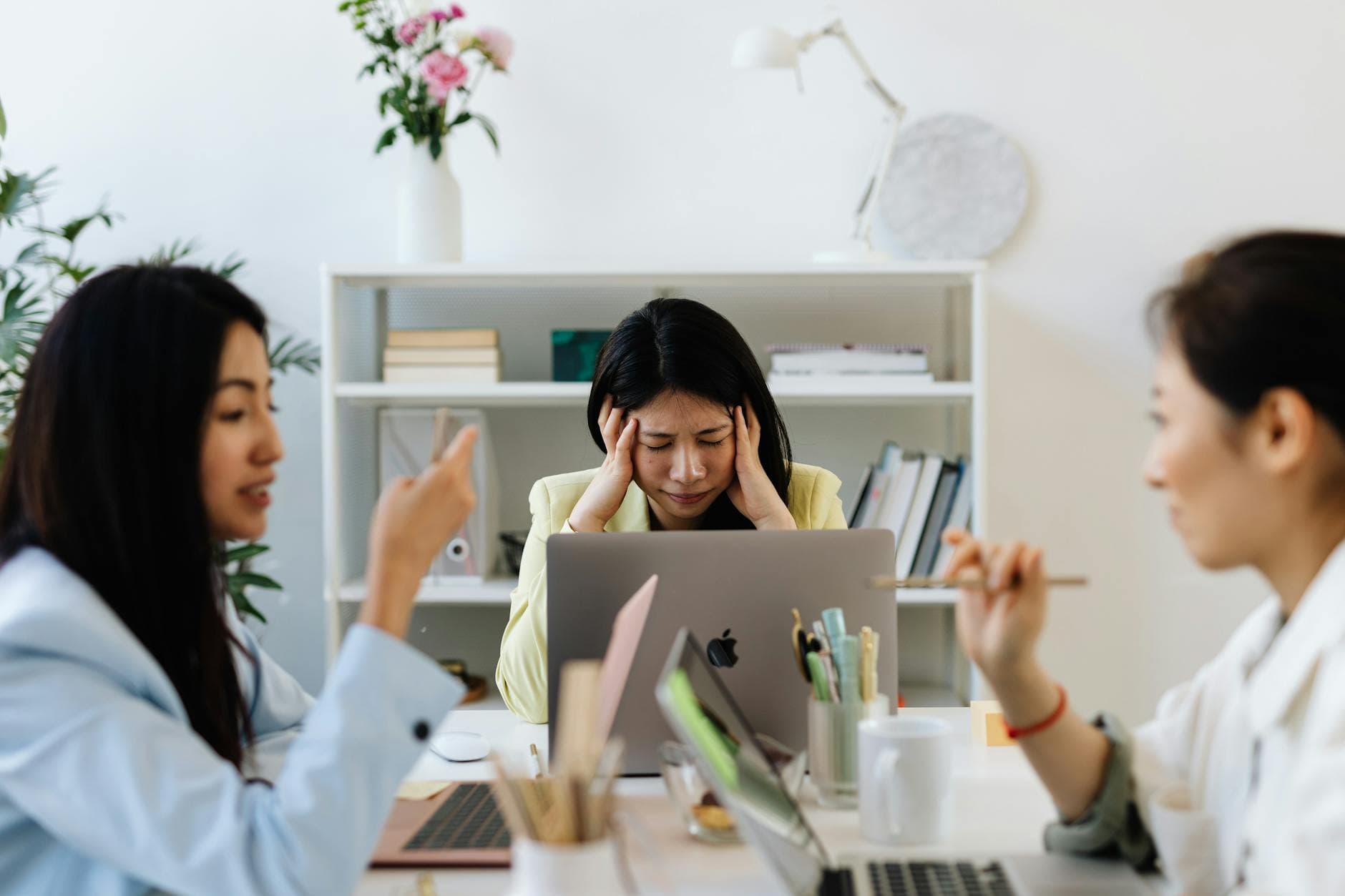 Asian businesswoman dealing with job stress in a modern office environment, surrounded by colleagues. - spring stress management