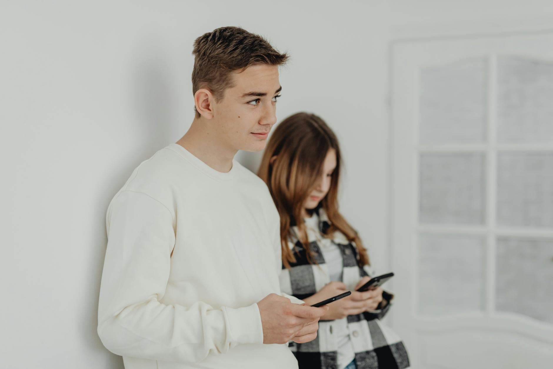 Two teenagers using smartphones, focusing on communication indoors. - teen social pressure