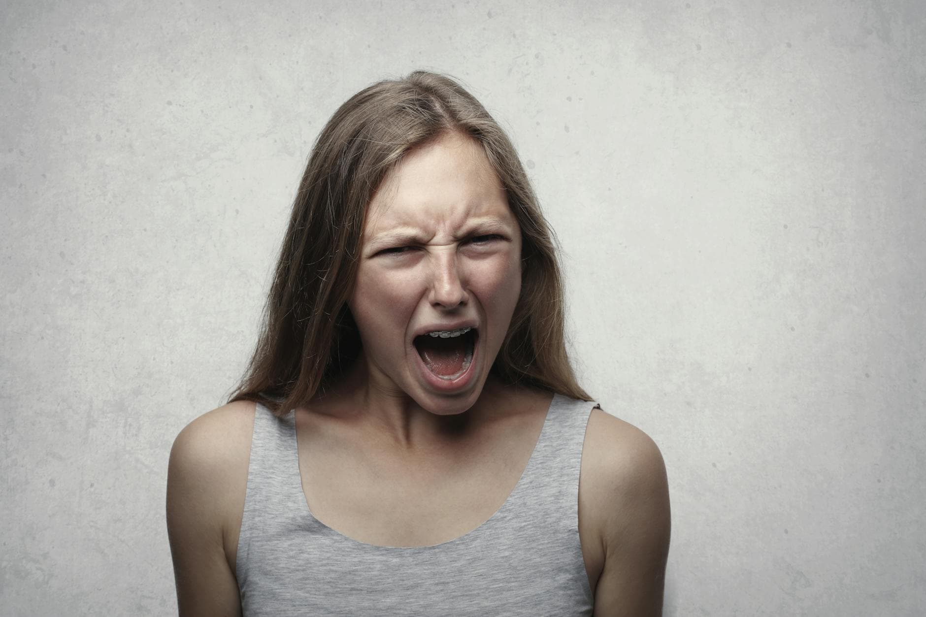 A woman with an intense facial expression screaming against a neutral gray background. - anger management cast