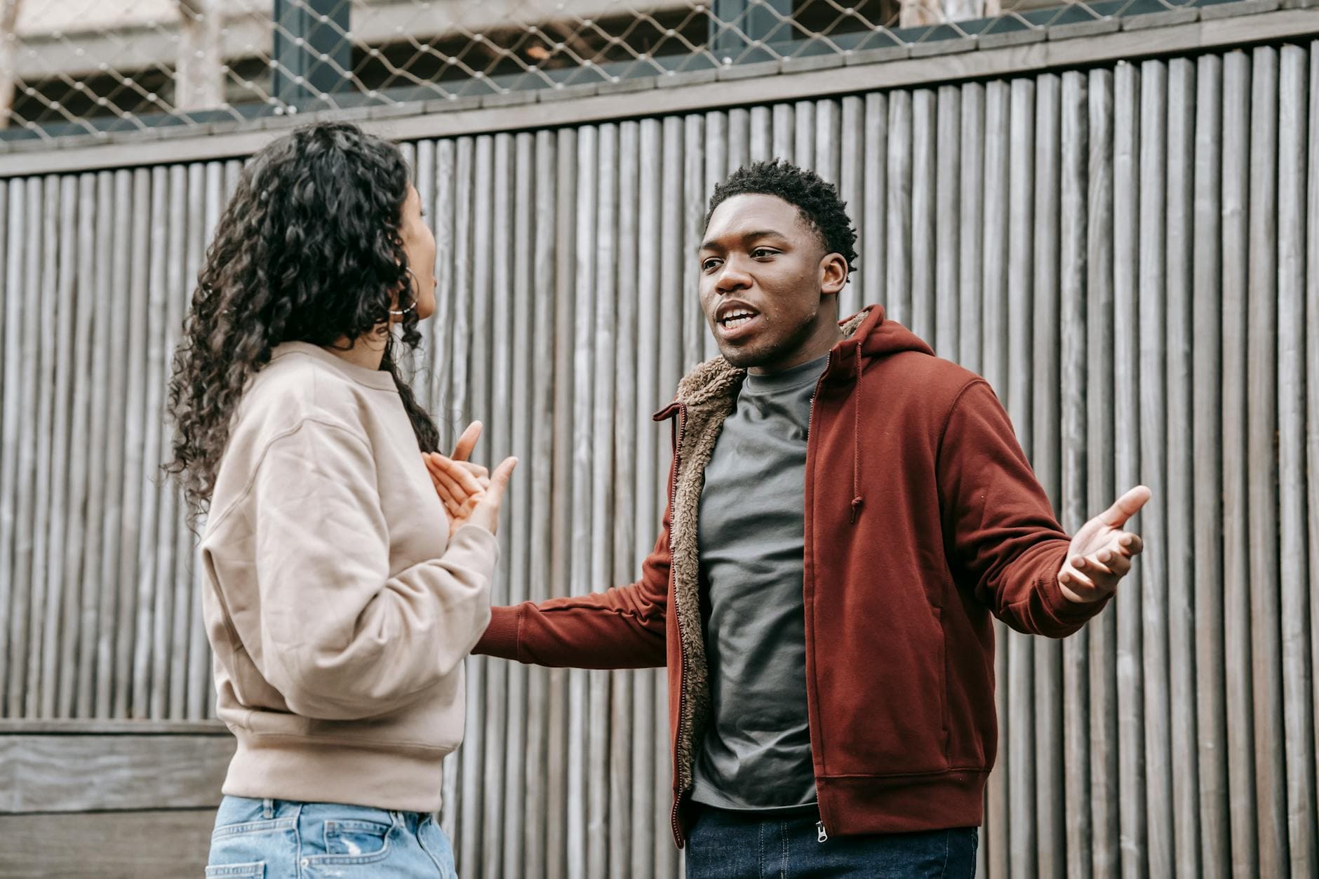 Angry African American boyfriend and ethnic girlfriend looking at each other while having emotional dispute on street near wooden fence - assertive communication in conflict