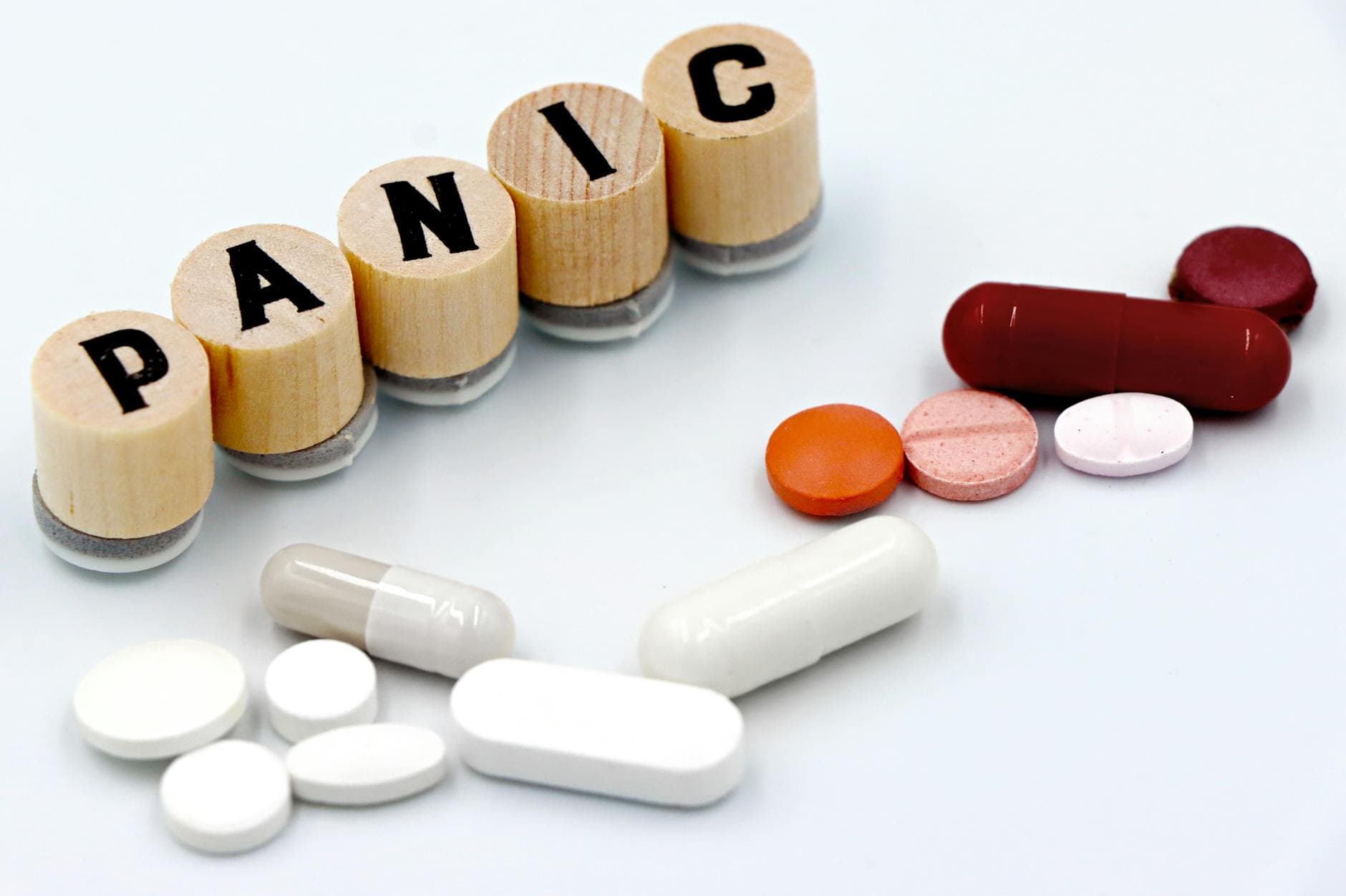 Assorted pills arranged beside wooden tiles spelling 'PANIC', symbolizing anxiety treatment. - what causes anxiety disorder