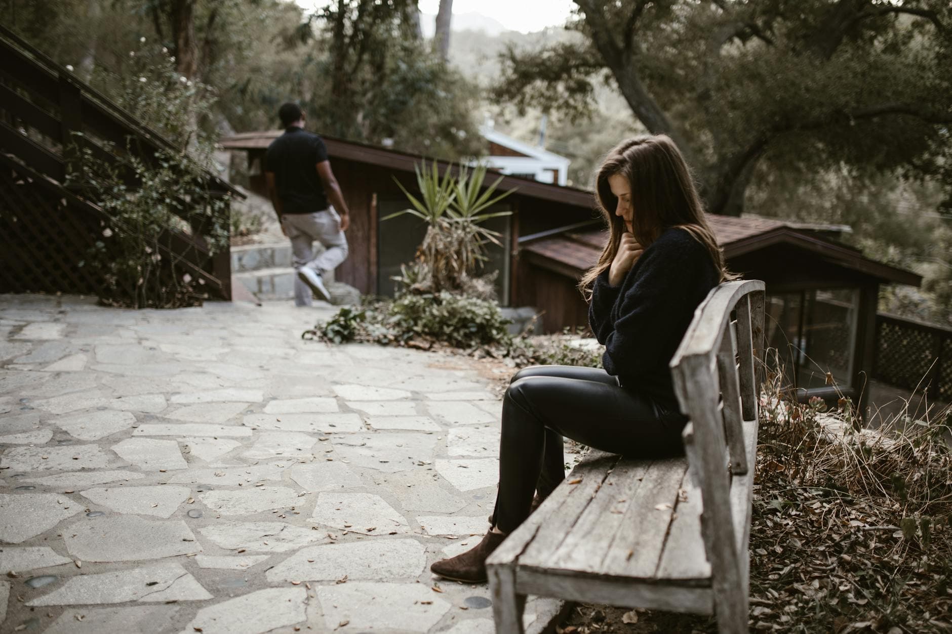 A woman sits pensively on a bench outside after a breakup, while a man walks away. - how to cope with breakup