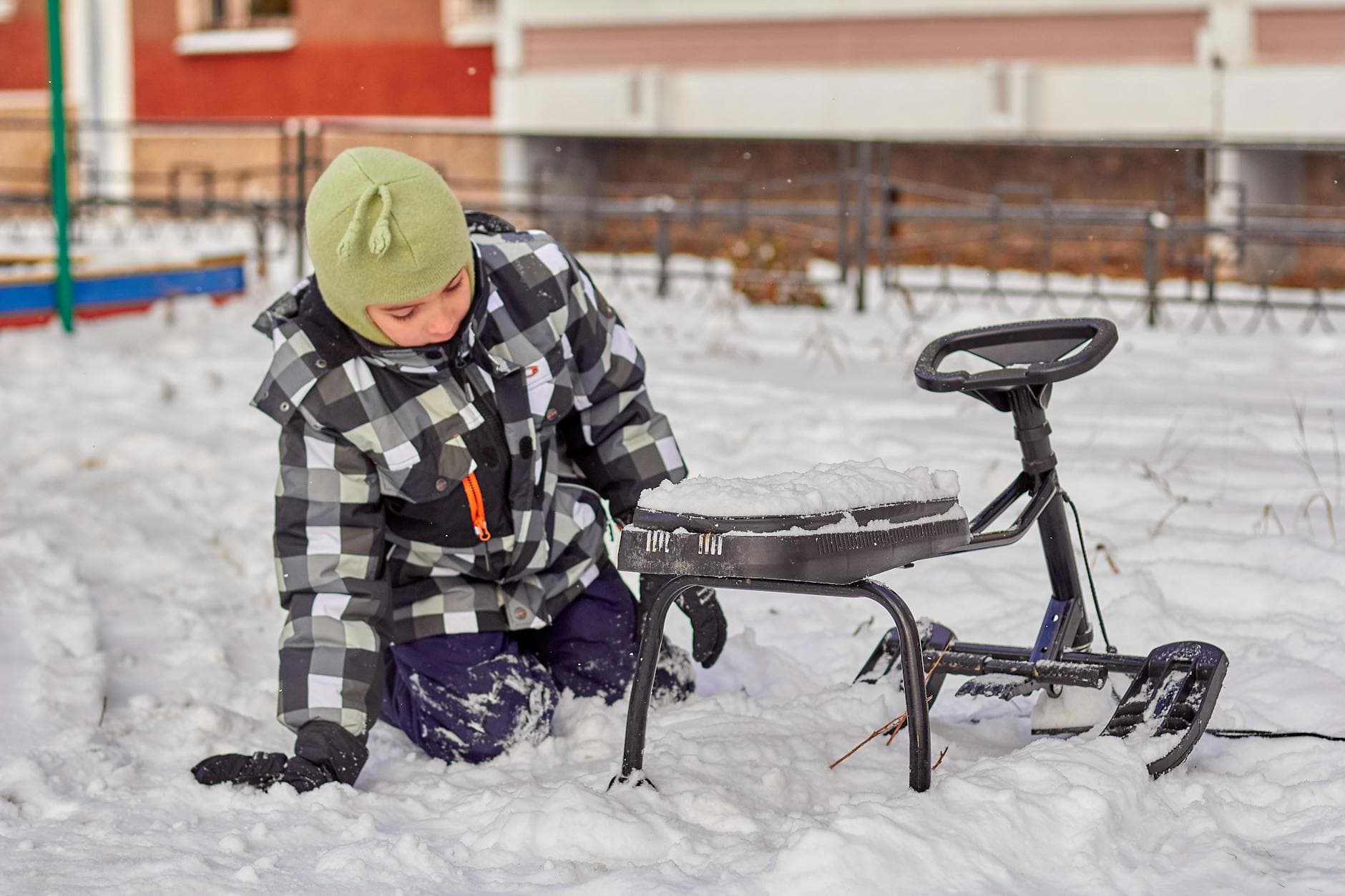 A child wearing winter attire plays with a sledge in a snowy outdoor setting. - creative indoor play snowy days