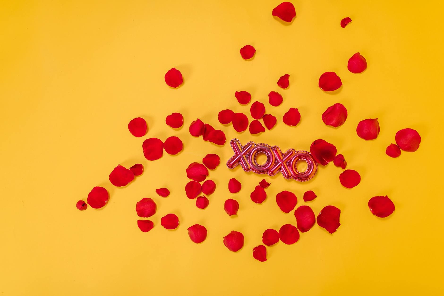 Red rose petals scattered with a XOXO sign on a vibrant yellow background. - creative valentine's day ideas