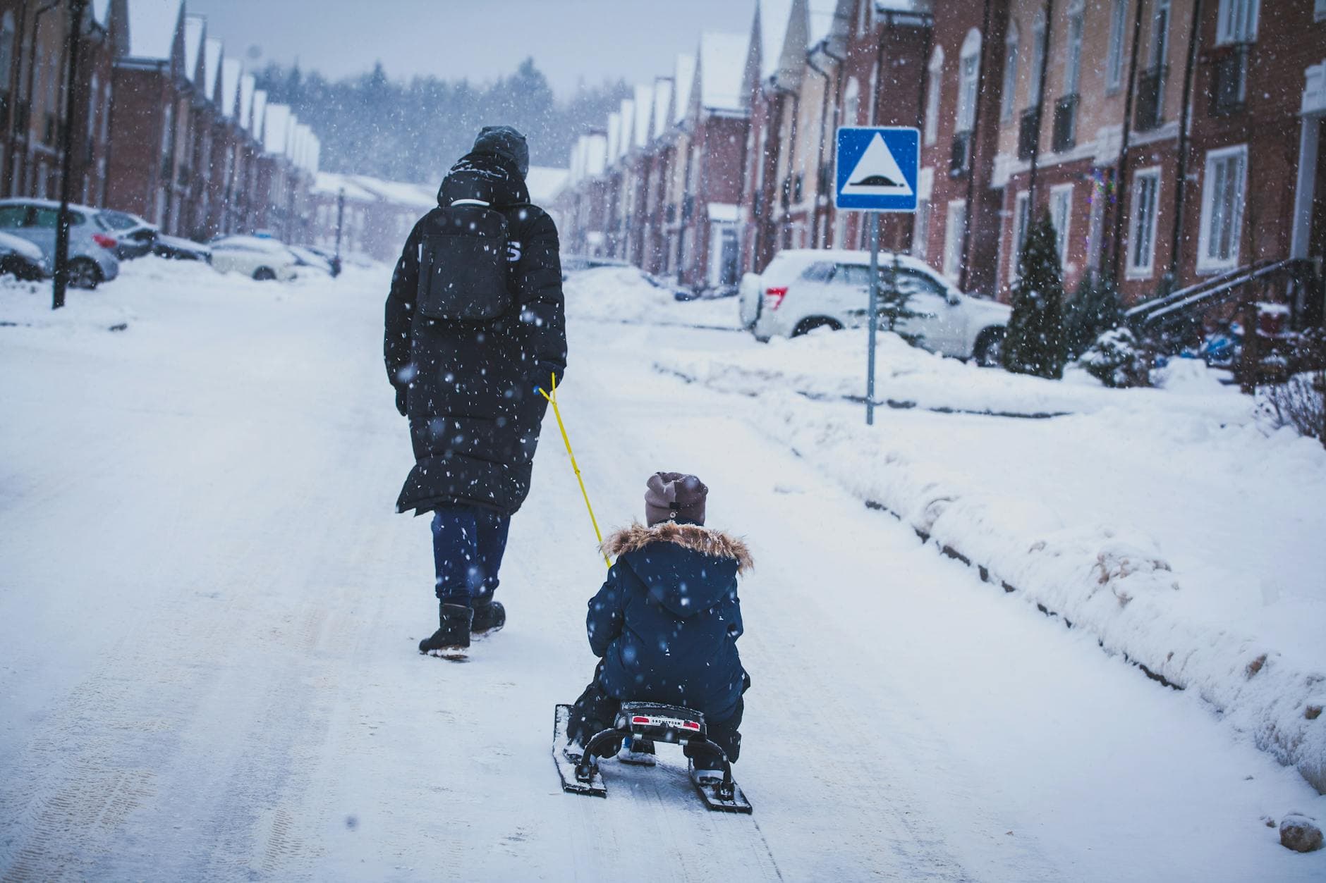 Child enjoying a winter sled ride on a snowy residential street with a parent nearby. - family snow day communication