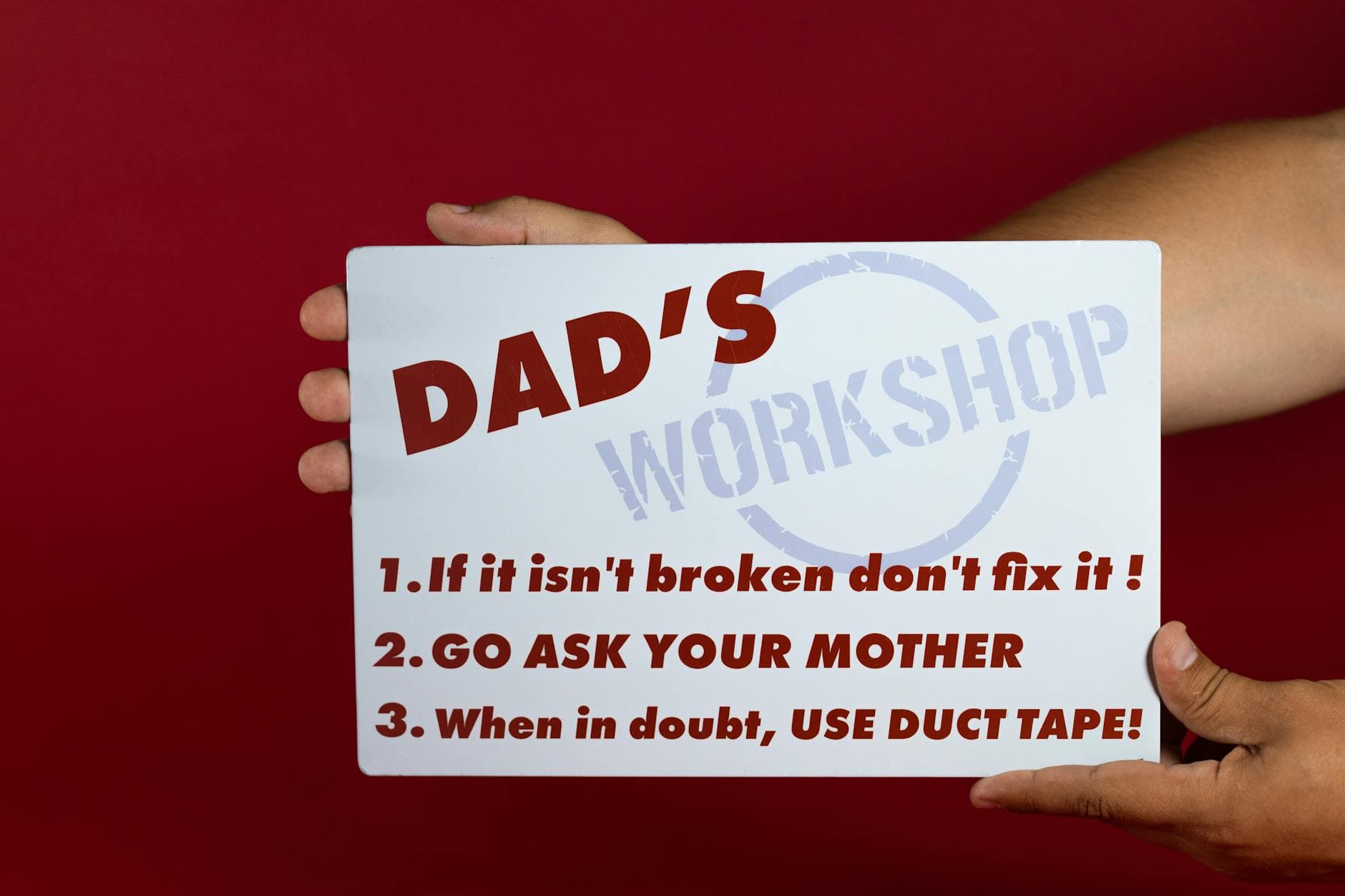 Close-up of a humorous sign with Dad's workshop rules on a red background held by hands. - funny marriage advice