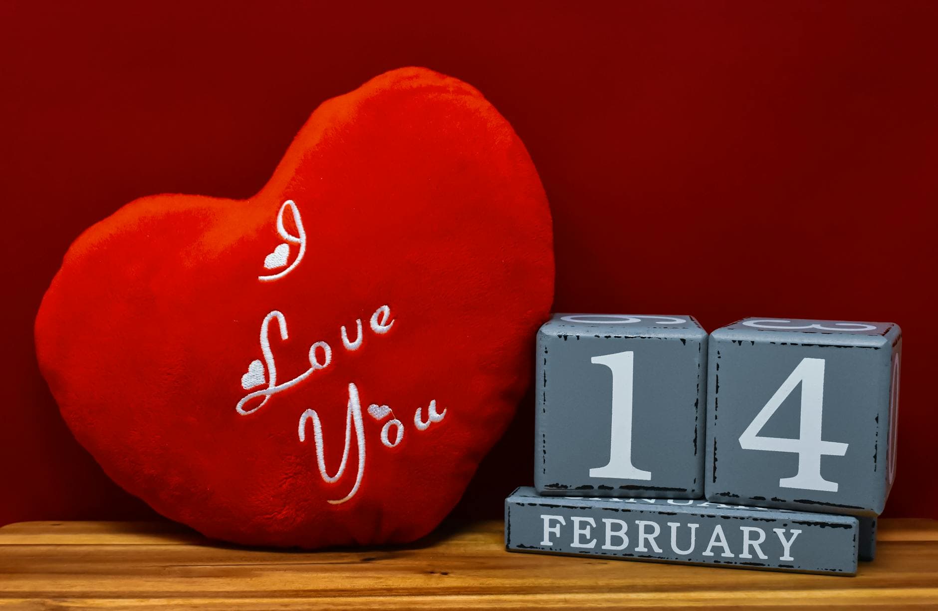 Red heart pillow with 'I Love You' text and February 14th blocks on wooden surface. - at home date ideas february