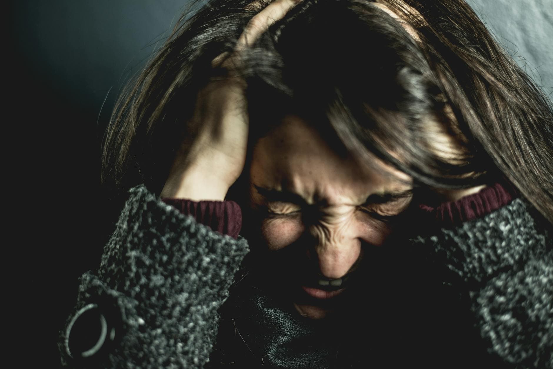 Close-up of a woman in distress with eyes closed and hands in hair, expressing anxiety. - mindfulness techniques financial stress