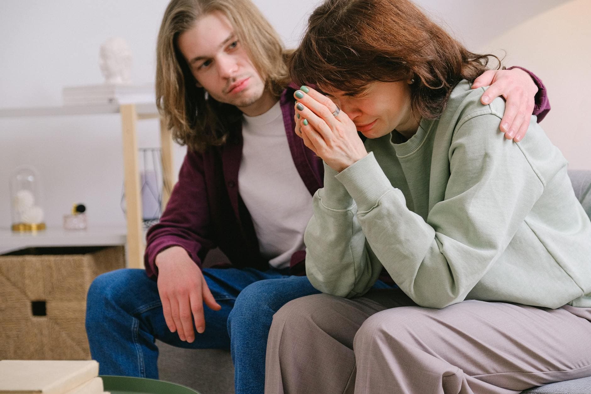 Crop male soothing disappointed crying female in sweatshirt and gray trousers on blurred background - post-holiday relationship regret