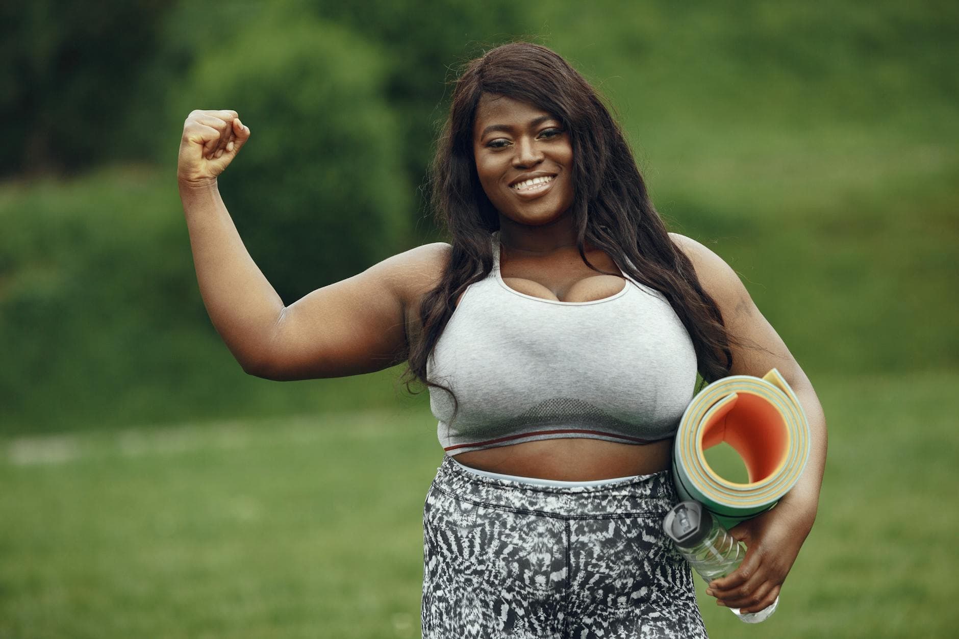 Smiling black woman holding a yoga mat, demonstrating strength in an outdoor setting. - self esteem building exercises