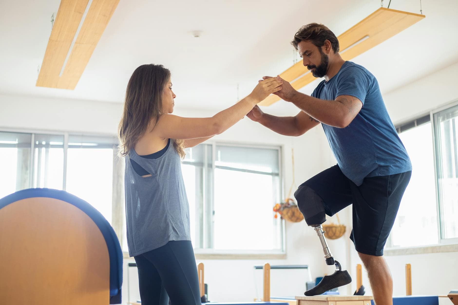 A man with a prosthetic leg exercises with a therapist in a well-lit gym environment. - winter therapy motivation