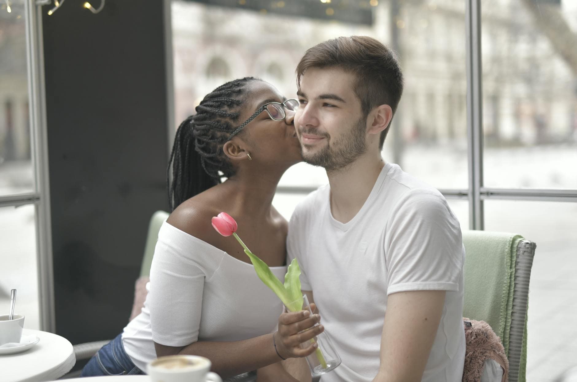 A multiracial couple shares a tender kiss while enjoying a coffee indoors, symbolizing love and intimacy. - how to apologize to a guy