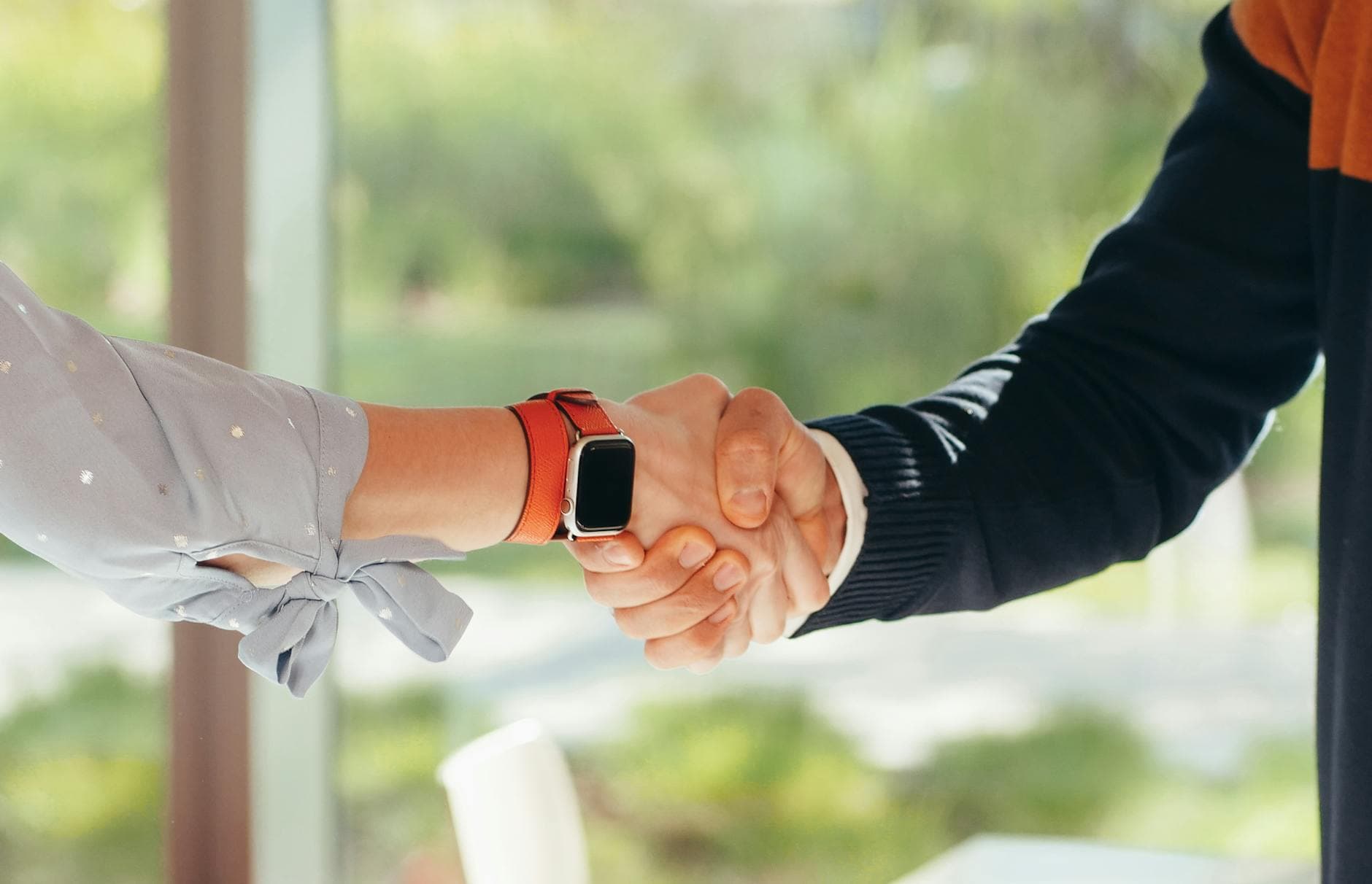 Close-up of a handshake between two adults, one wearing a smartwatch, set in an outdoor environment. - build trust relationships