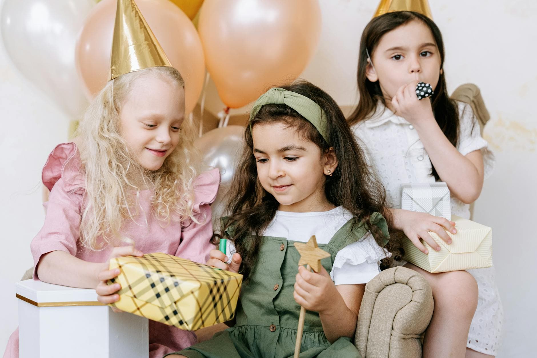 Three young girls celebrate a birthday with gifts, balloons, and party hats, capturing a moment of joyful togetherness. - childhood meltdowns