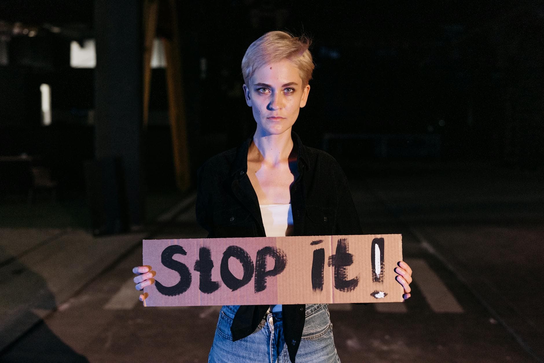 A woman holds a bold protest sign reading 'Stop it!' in a nighttime setting. - gaslighting signs
