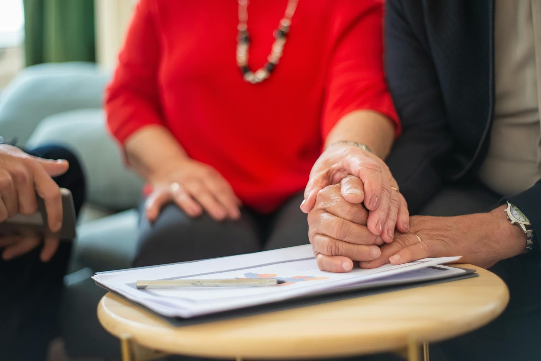 Senior couple holding hands over a table with documents, symbolizing support in an office setting. - midlife relationship counseling