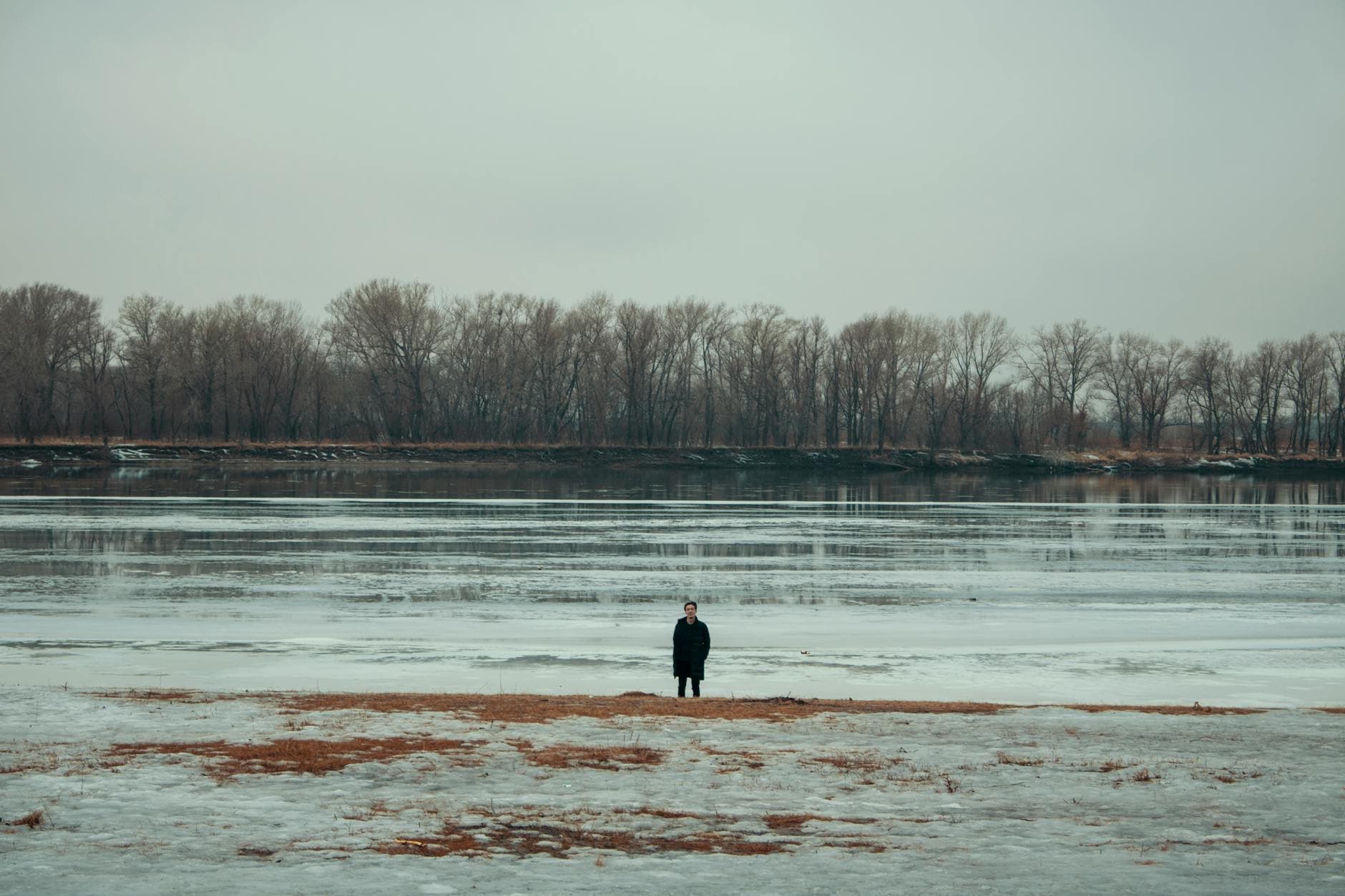 A lone person standing by a frozen river with trees in the background during winter. - overcome loneliness winter