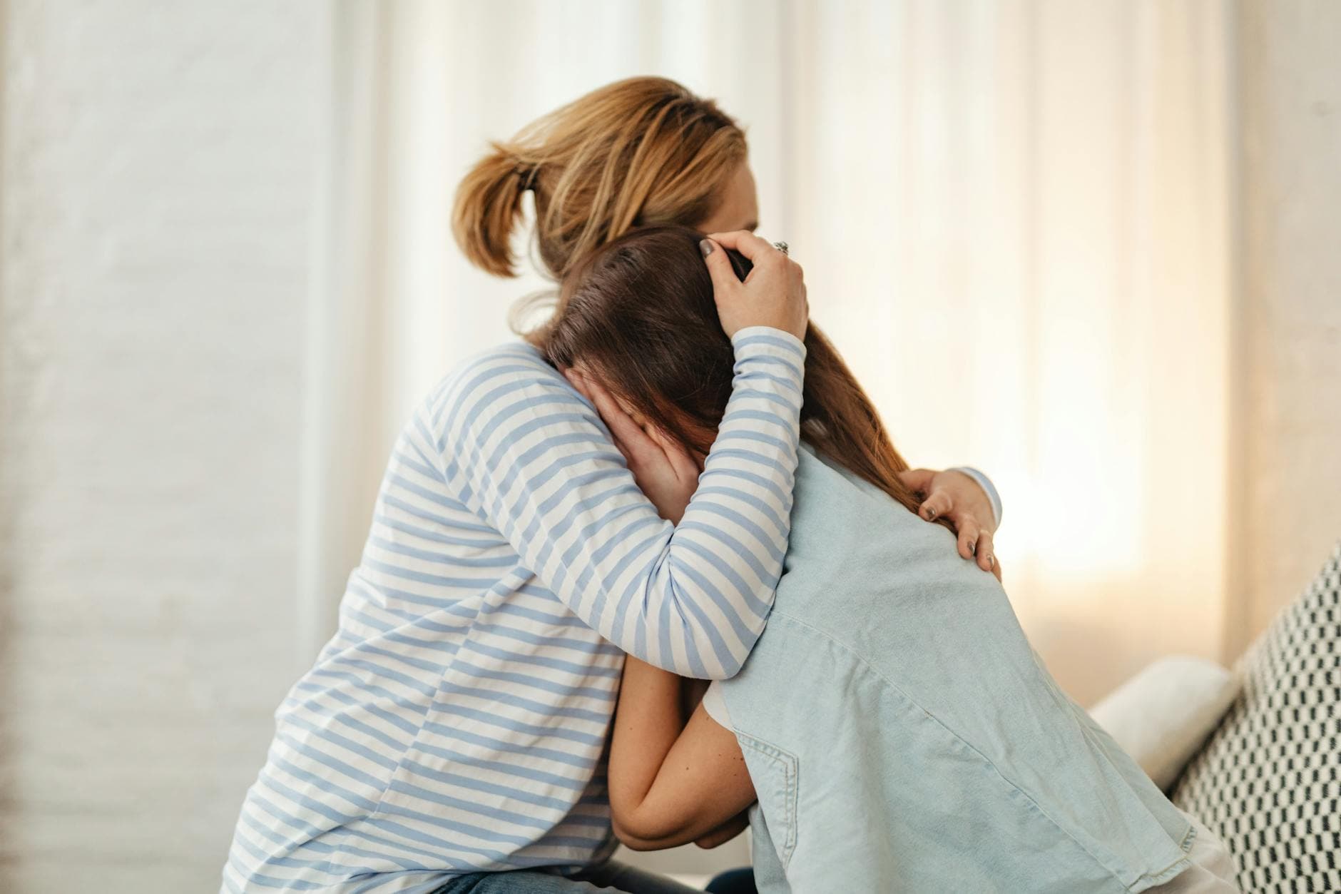A mother lovingly comforts her teenage daughter in an emotional embrace indoors. - parental emotional support