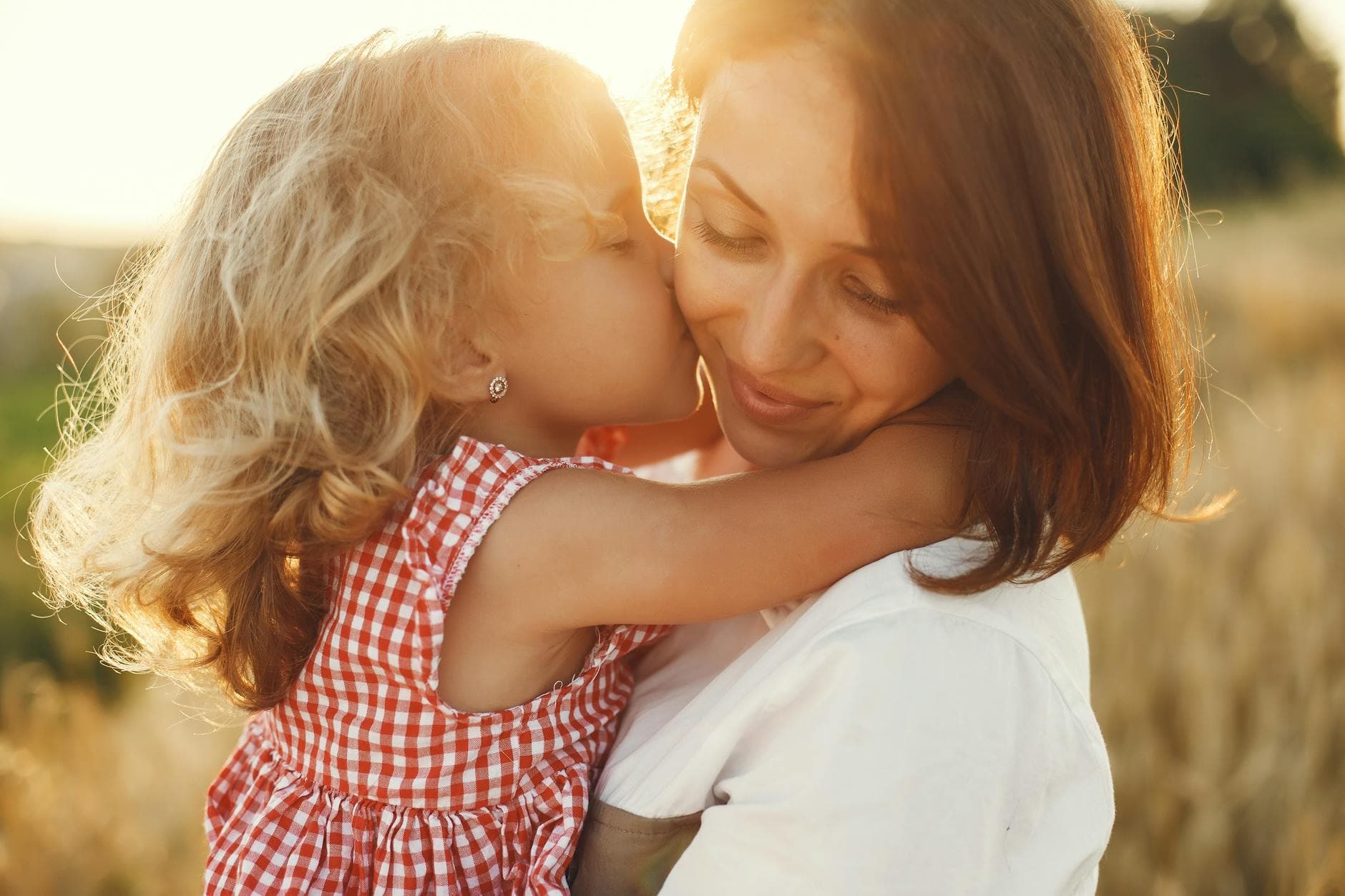 A young girl lovingly kisses her mother in a sunlit field, expressing warmth and affection. - post divorce co parenting