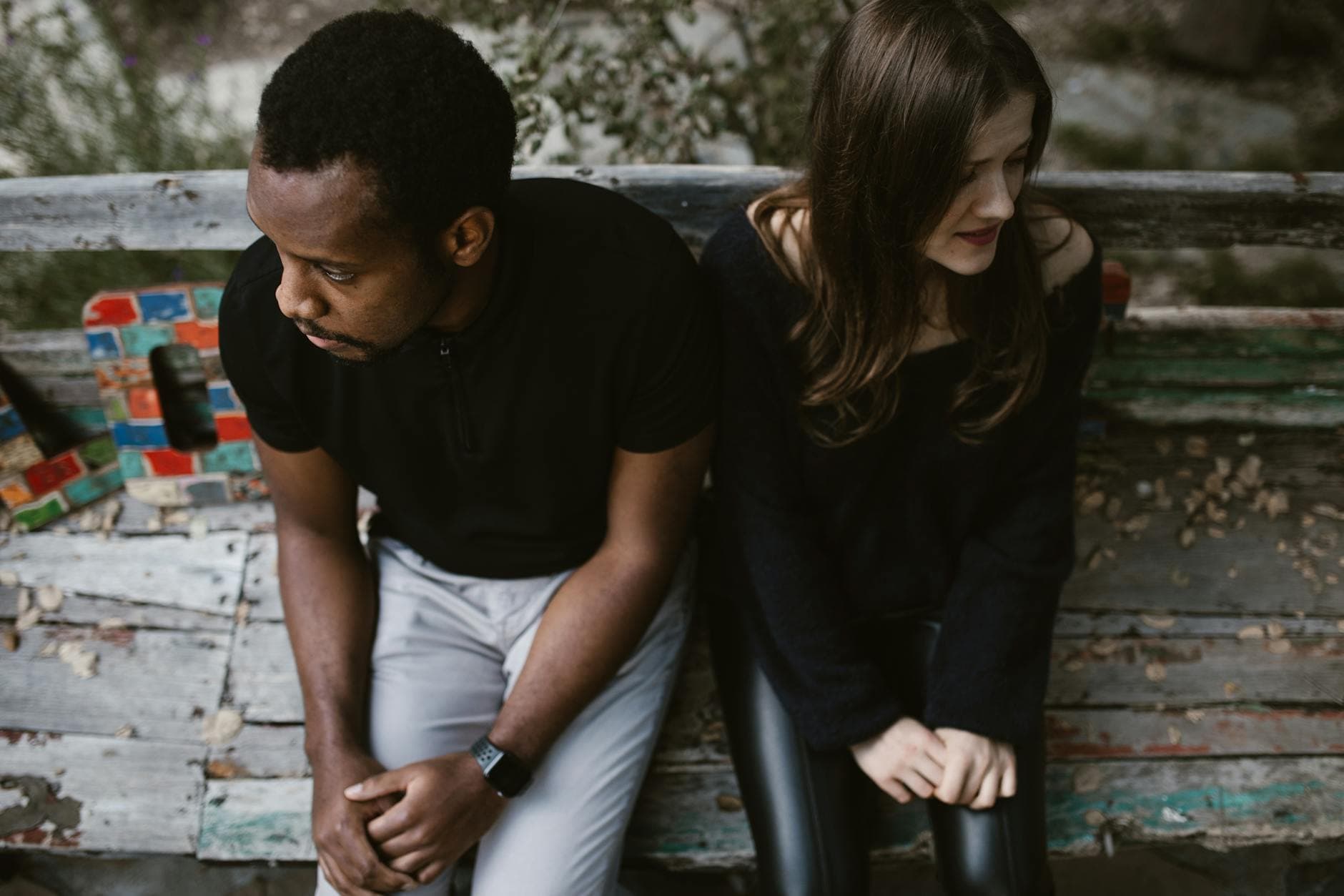 A couple sitting apart on a park bench, expressing emotions. Outdoors setting. - post holiday relationship challenges