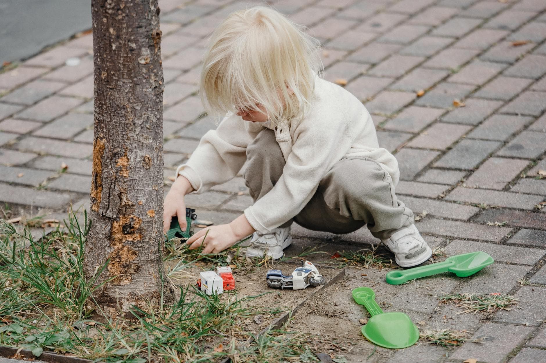A young child engaged in imaginative play with toy cars and a shovel outdoors on a bright day. - preschool nature activities