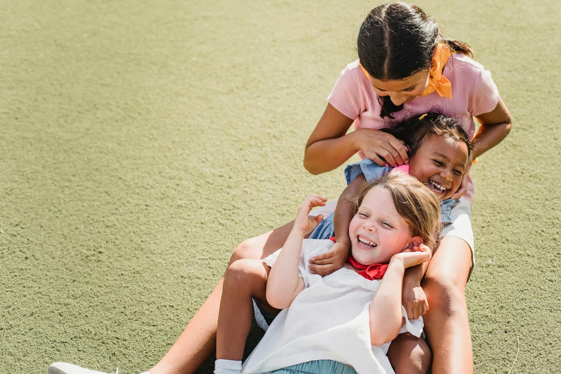 Three children laughing and playing together on grass under the sunny sky, showcasing pure joy and friendship. - preschool playdate etiquette