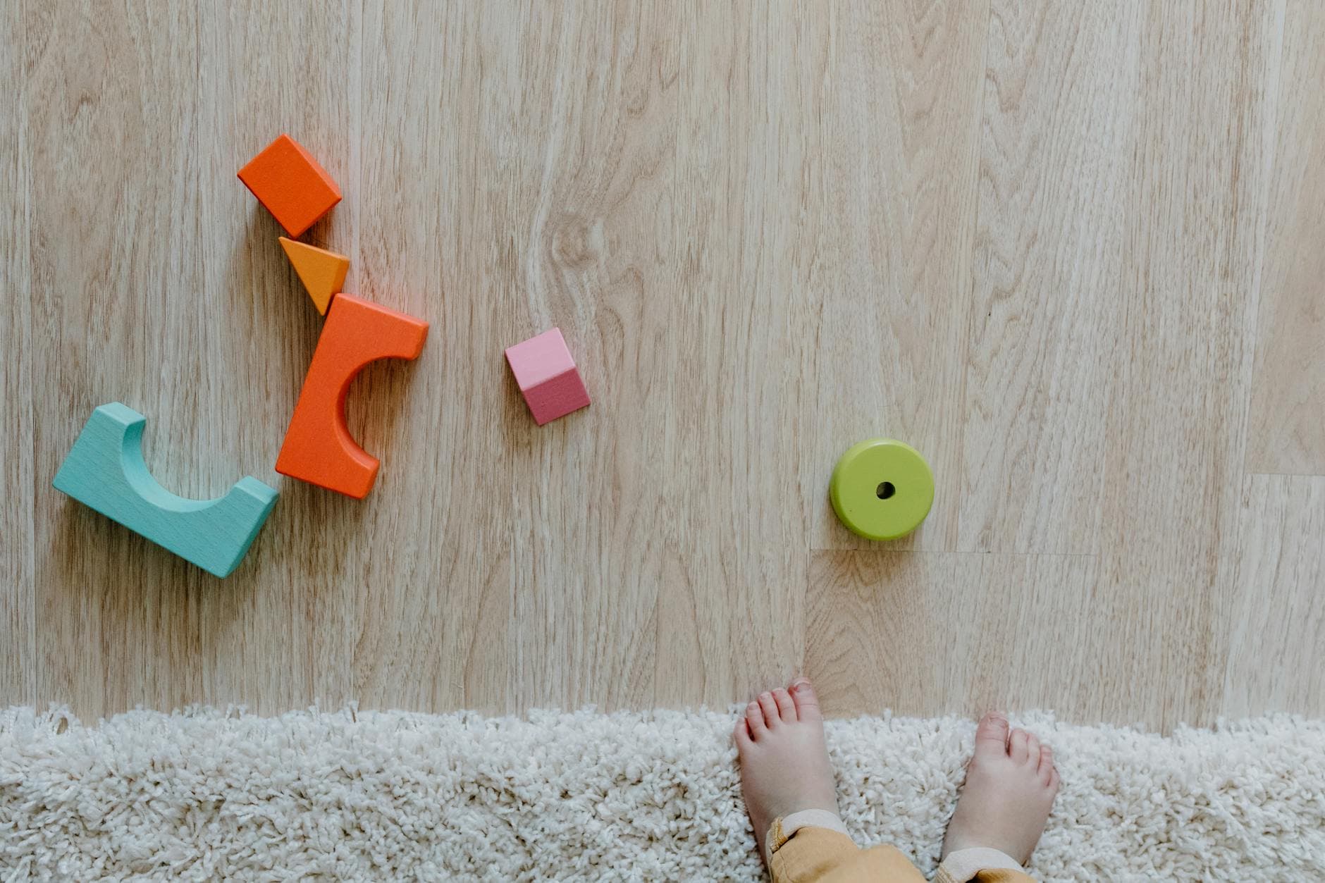 Colorful wooden blocks and baby feet on a carpet and wooden floor, emphasizing child's early playtime. - preschooler independence