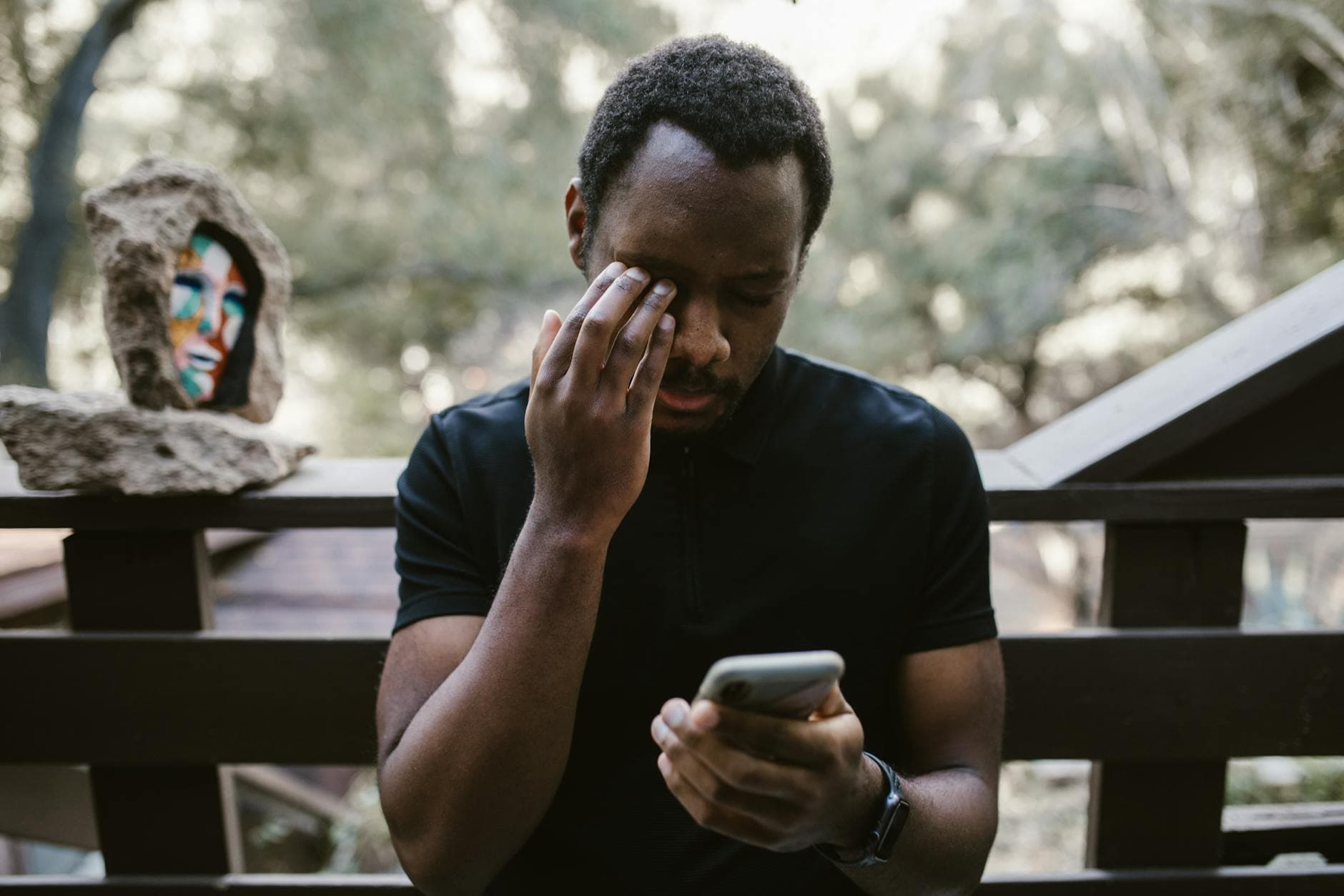 A man stands on a balcony outdoors, holding a smartphone, deep in thought. - sad spring treatment