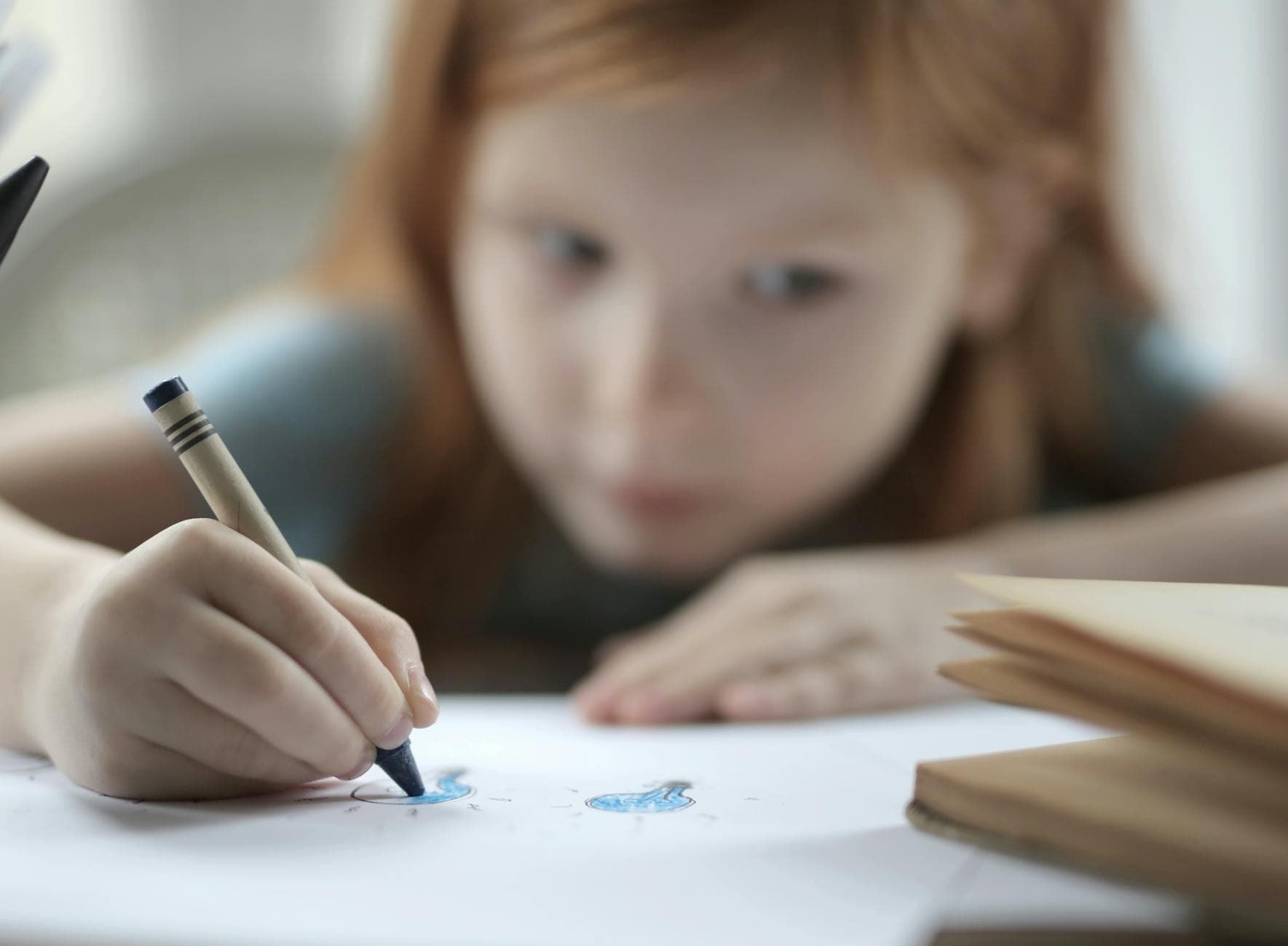 A young girl concentrates on coloring in a classroom with a blue crayon, fostering creativity. - school closure activities